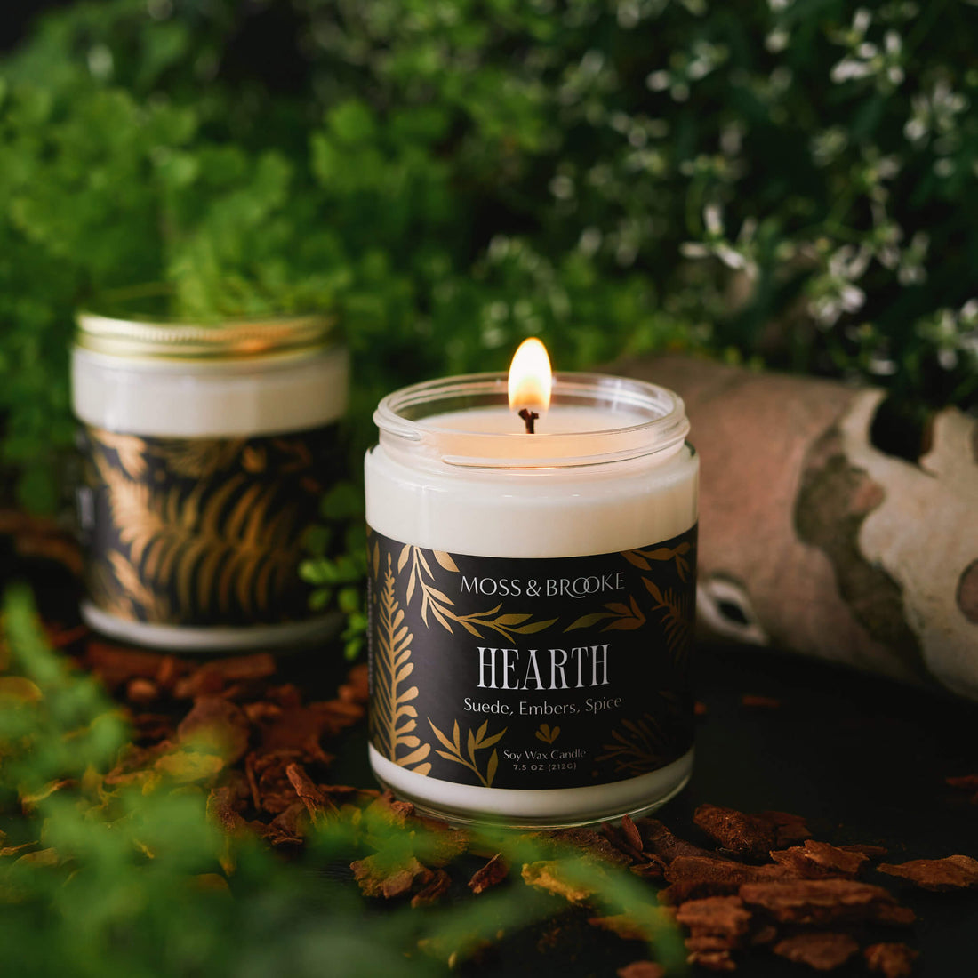 Soap rebranding case study image of Moss & Brooke range of candles in a dark moody background. The glass jars feature black labels with gold botanical detailing and ornate typography.
