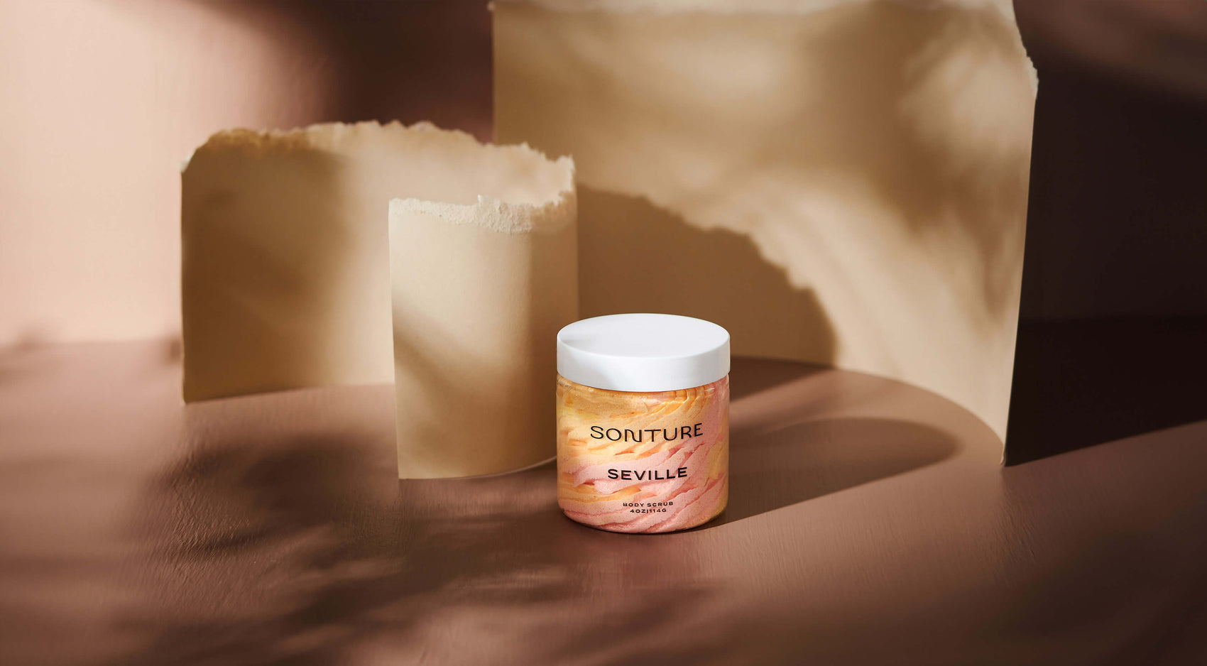 Skincare brand design portfolio image of the Sonture body butter in a styled brown setting, torn paper behind. The very minimal label creates a minimal, high end feel and contrasts the colourful product. 