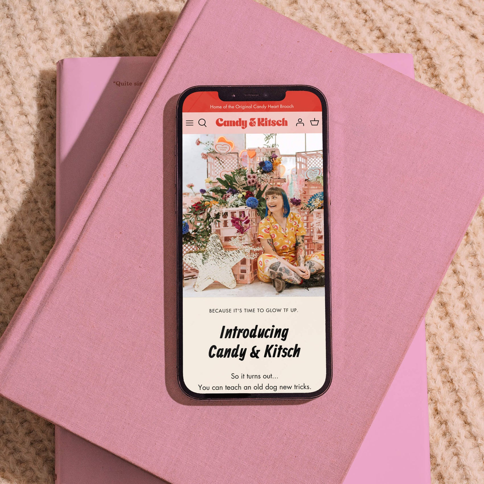 A thumbnail of my brand design portfolio of the Candy & Kitsch website. It shows a phone on top of a stack of pink books on a knitted blanket.