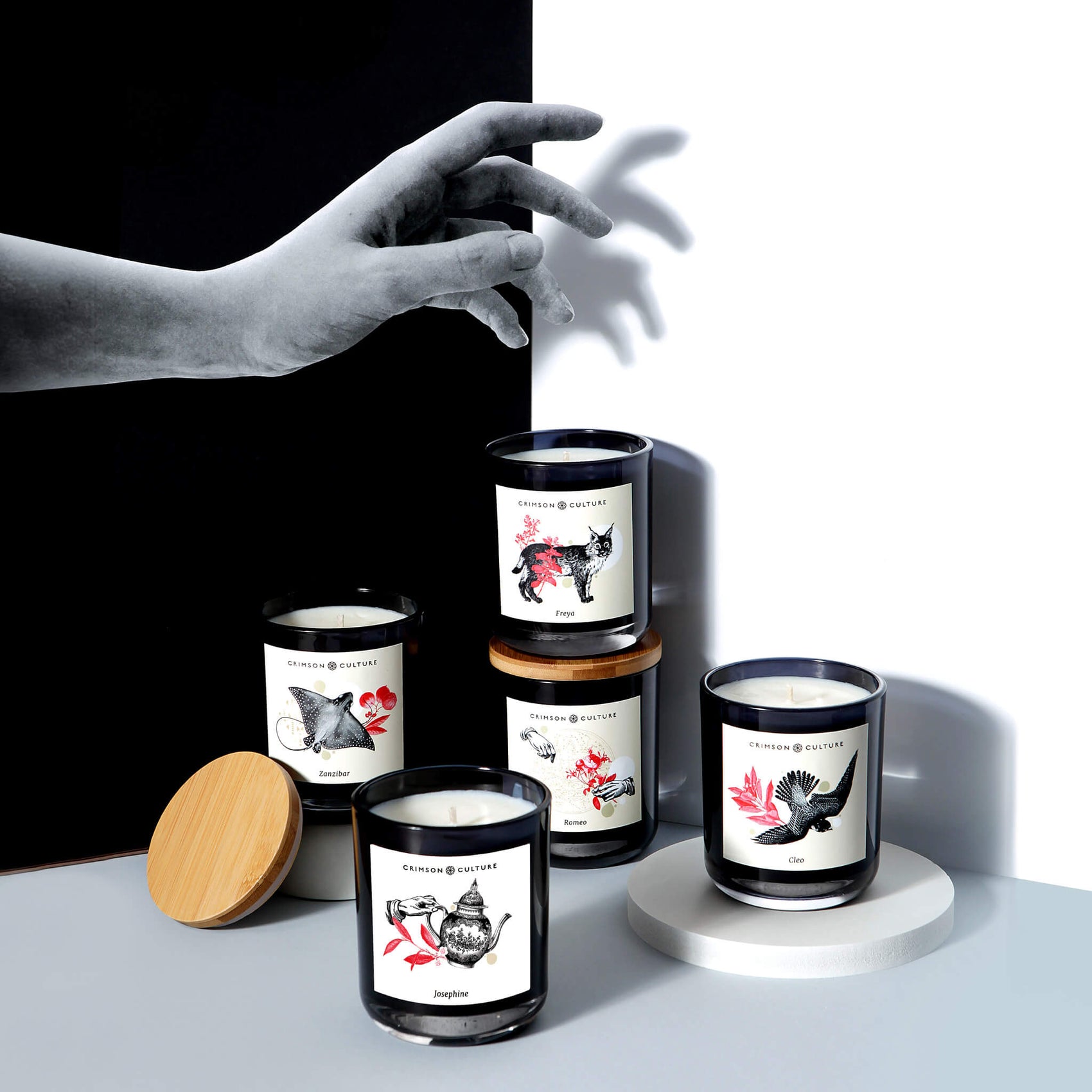 Candle brand identity case study image of the Crimson Culture candle range. The styled image features a black and white background with the arranged candles being reached at by a cut out paper hand. 
