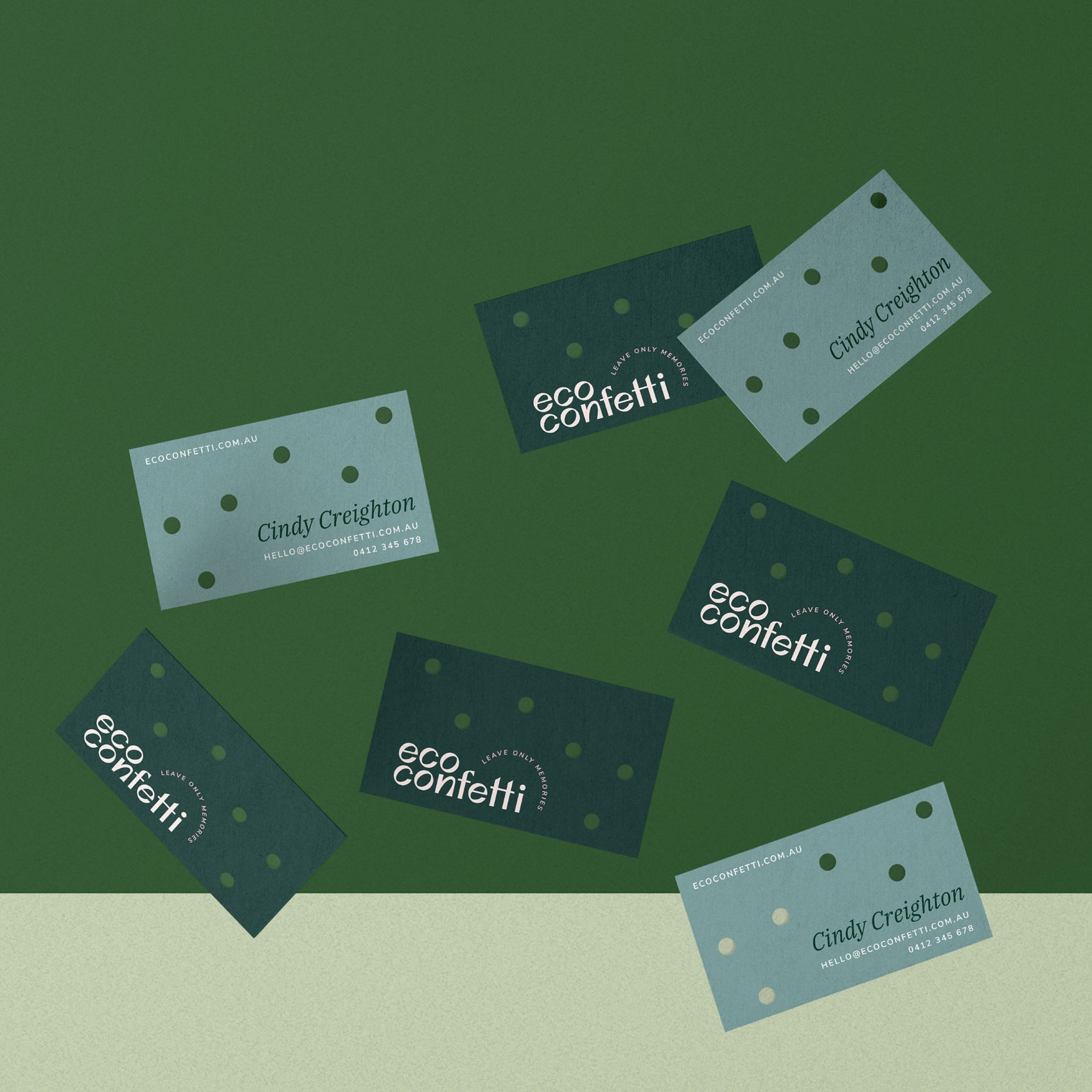 Sustainable brand design portfolio image of Eco Confetti business cards floating in a scene. The cards feature small diecut holes (to suggest the creation of confetti!) with a dark green front showing the logo and aqua back holding founder Cindy’s details.