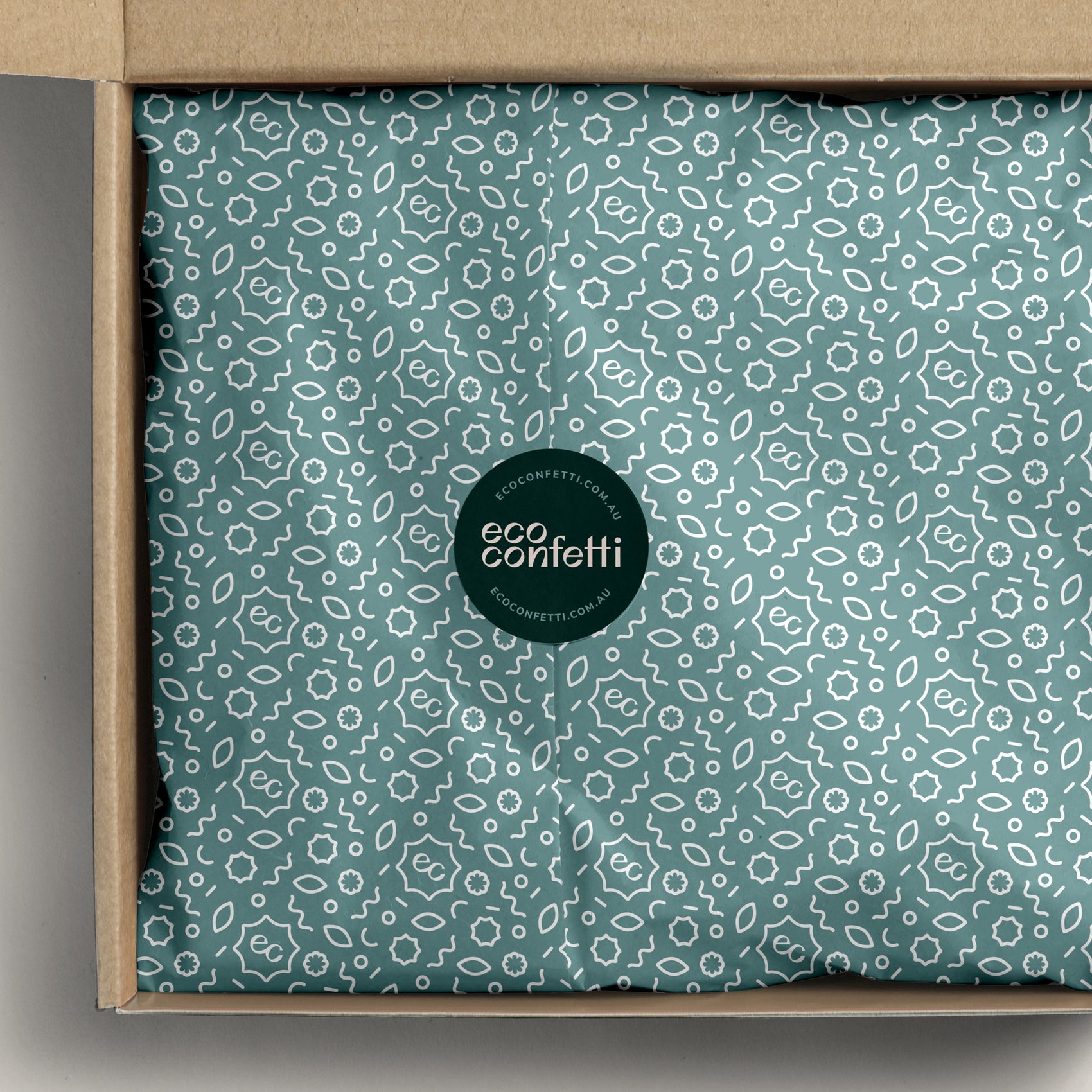 Sustainable brand identity case study image of the Eco Confetti custom tissue paper in a box. The light aqua design features the brand icon and supporting shape graphics in white with a green sticker with the logo sealing the package. 