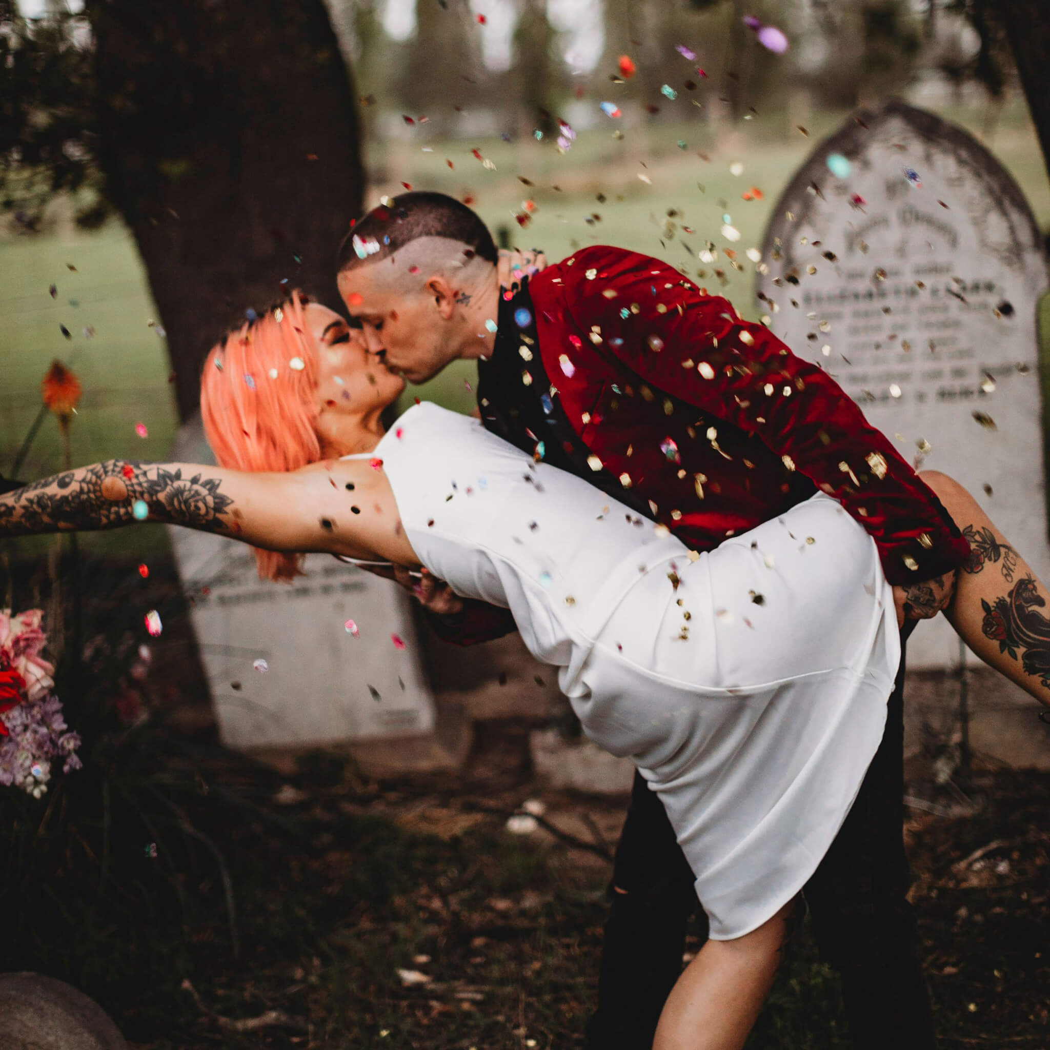 Sustainable brand design portfolio image featuring brand photography for Eco Confetti. A punk-styled couple dip and kiss in a graveyard, gold glitter-y confetti surrounding them. 