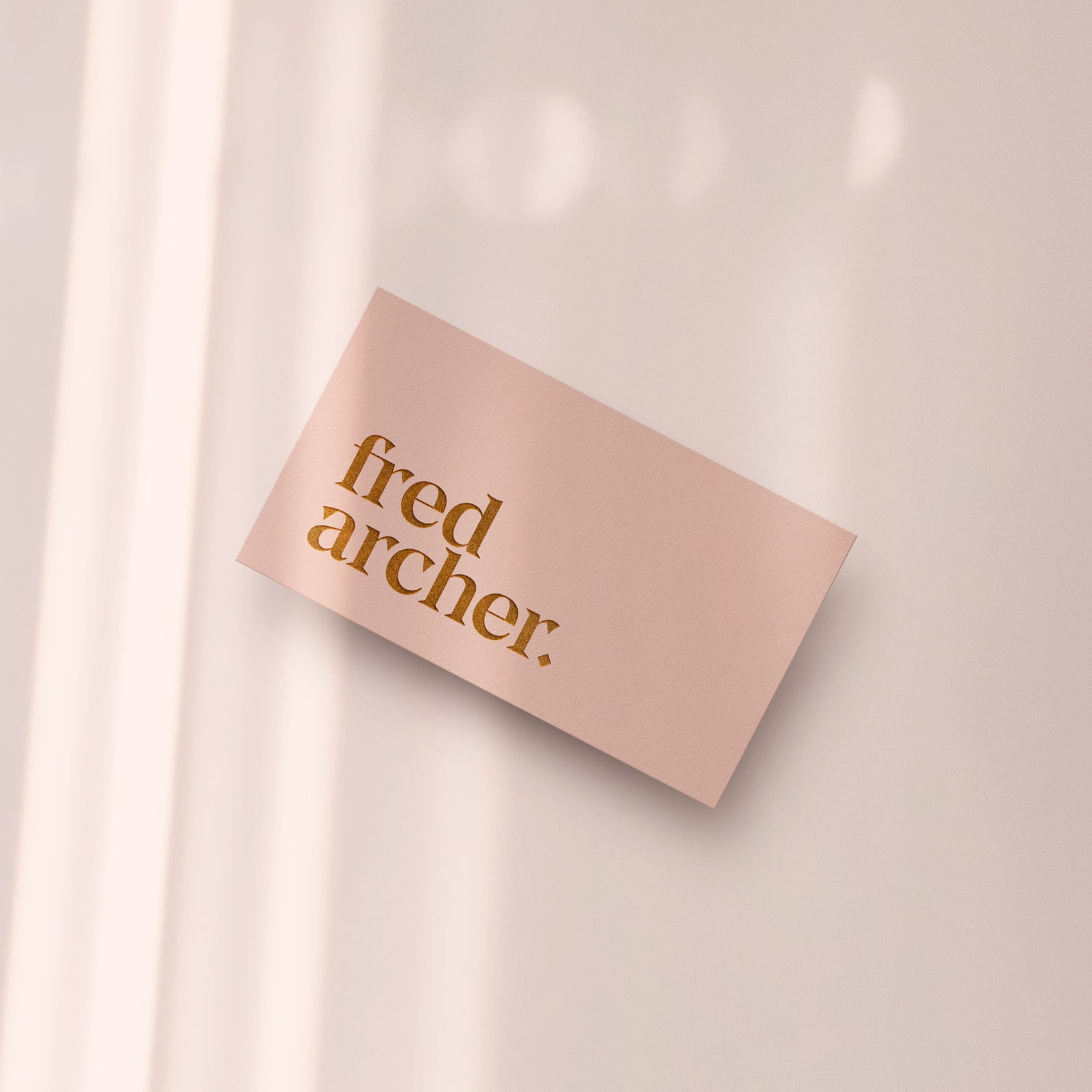 Fashion designer brand design portfolio image of the Fred Archer business cards. The light blush front features the sharp serif logotype in a rose-gold pink foil.