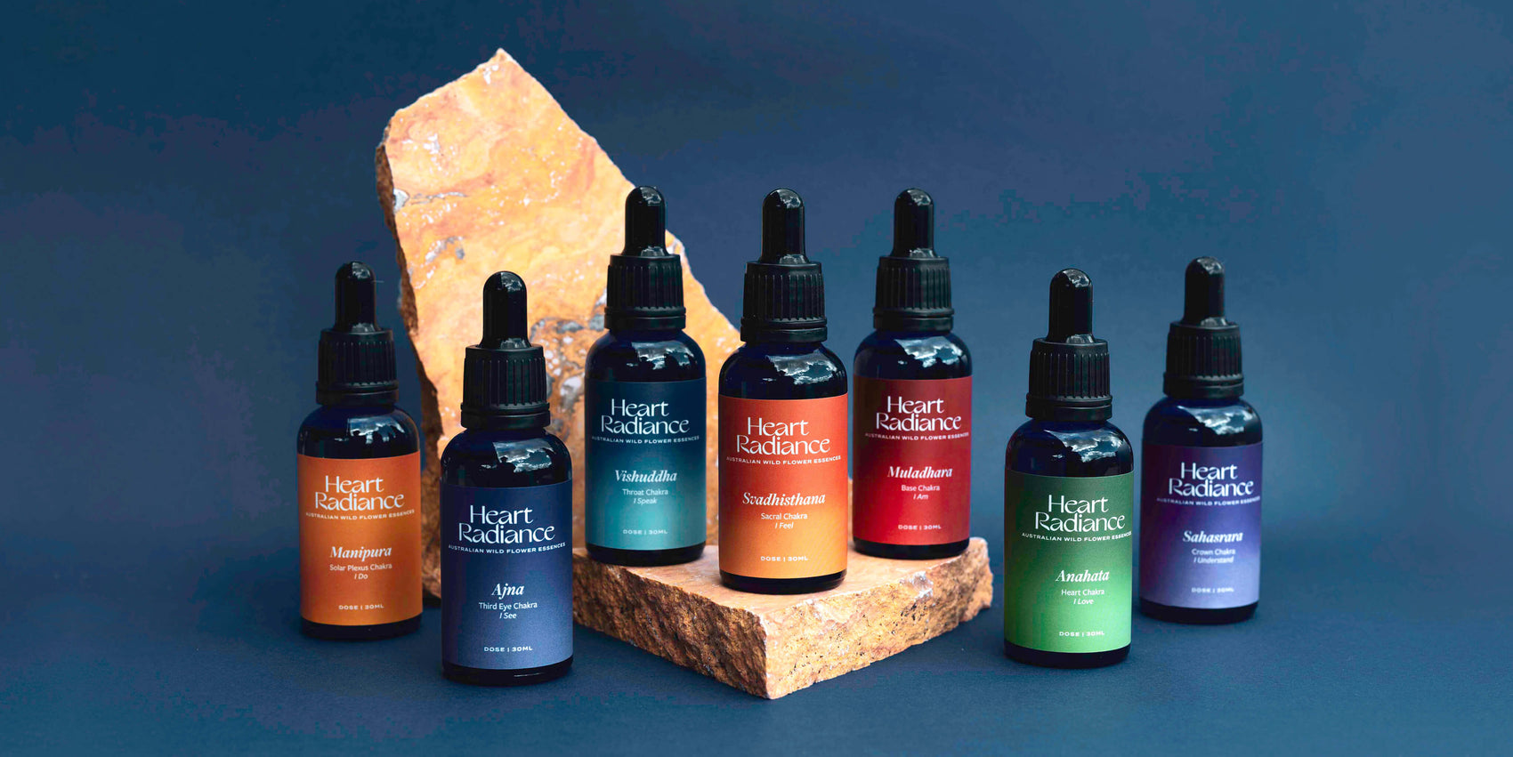 Rebranding case study image of the HeartRadiance brand of chakra spray mists on a stone in a deep blue background. The blue glass dropper bottles feature rich colours and form a rainbow.