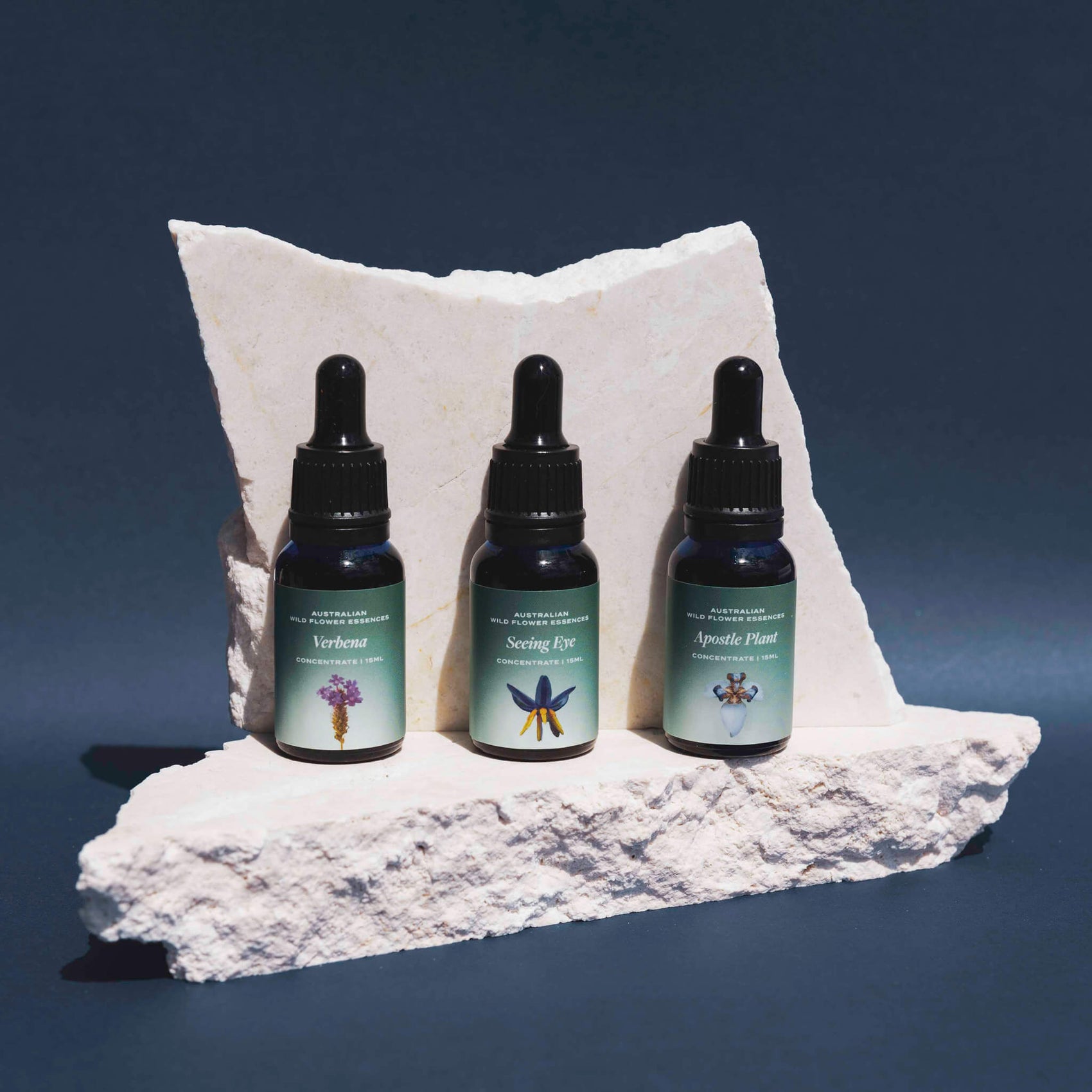 Brand identity case study image of three HeartRadiance dropper bottles on a white stone in front of a green blue background. The product labels feature hazy blue/green gradients and elegant white typography alongside an image of each flower.