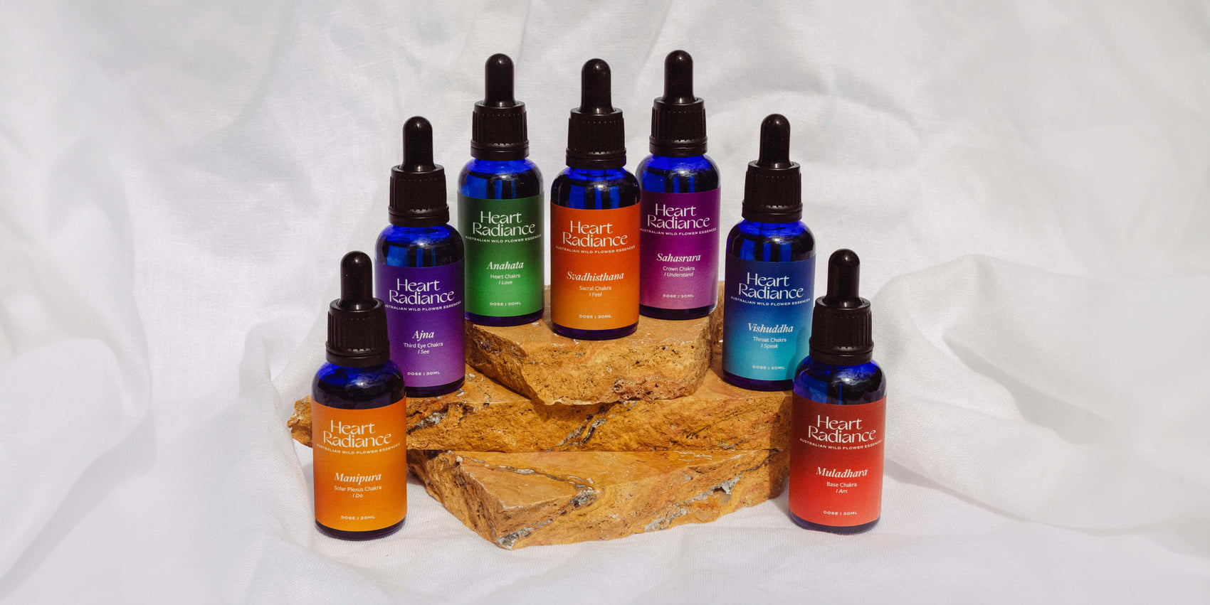 Rebranding case study image of the HeartRadiance brand of chakra spray mists on a stone in front of a white background. The blue glass dropper bottles feature rich colours and form a custom label rainbow.