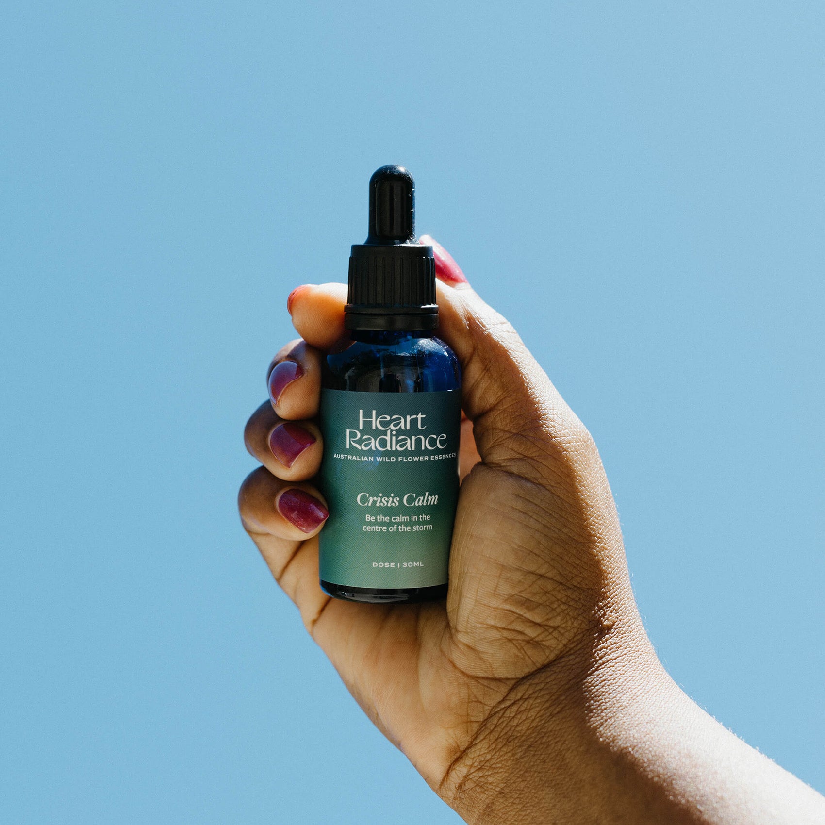 Rebranding case study image of a deep-skin toned hand holding a bottle of HeartRadiance essence. The custom product label features hazy blue/green gradients and elegant white typography. 