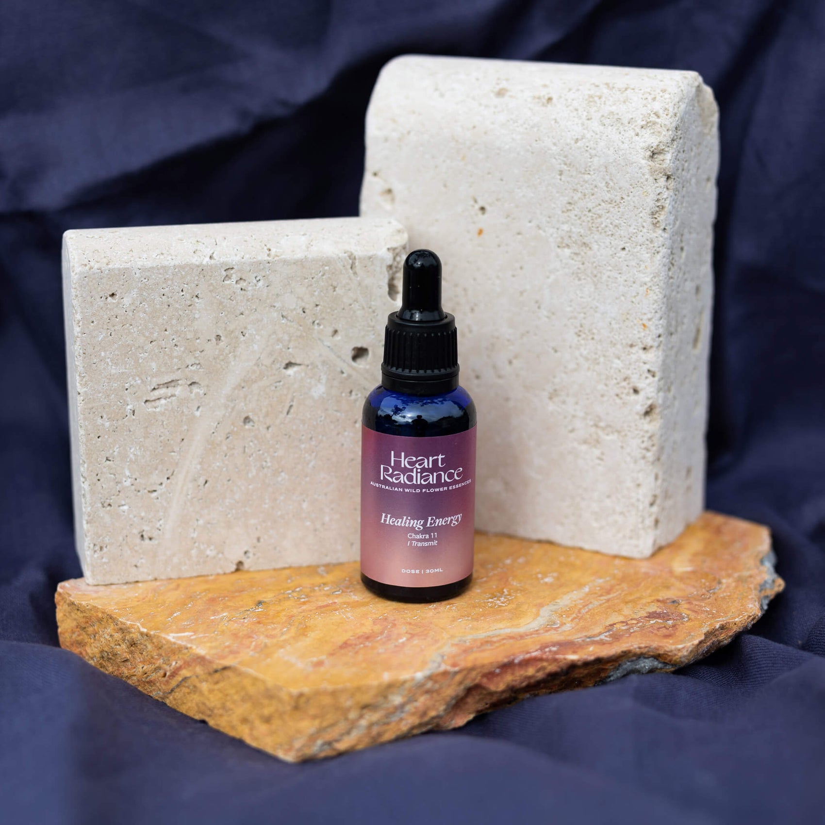 Rebranding case study image of a shiny upper chakra flower essence for HeartRadiance sitting on stones in blue setting. The blue glass bottle features a metallic light pink gradient with clean white typography. 