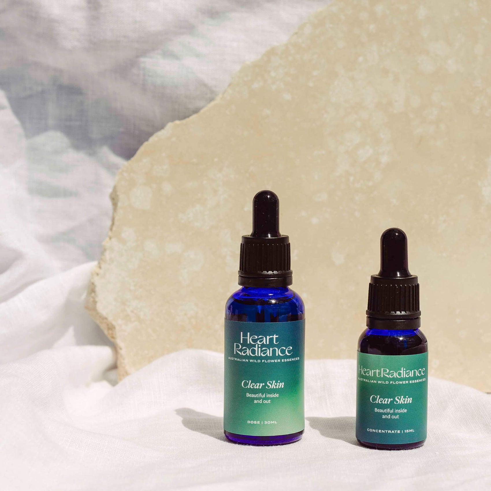 Brand identity case study image of two HeartRadiance dropper bottles in front of stones in a rich blue background. The custom product labels feature hazy blue/green gradients and elegant white typography. 