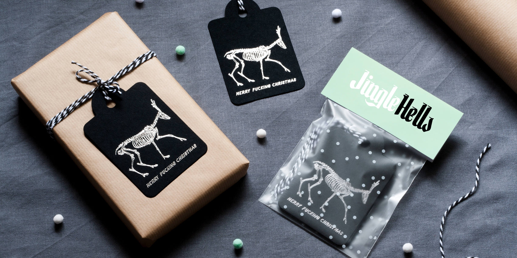 Stationery brand design example for personal design project Jingle Hells. On a grey background sits the custom silver foil gift tags with skeletonised deer. A gift is wrapped in brown paper and sits next to the tag and packaged product. 