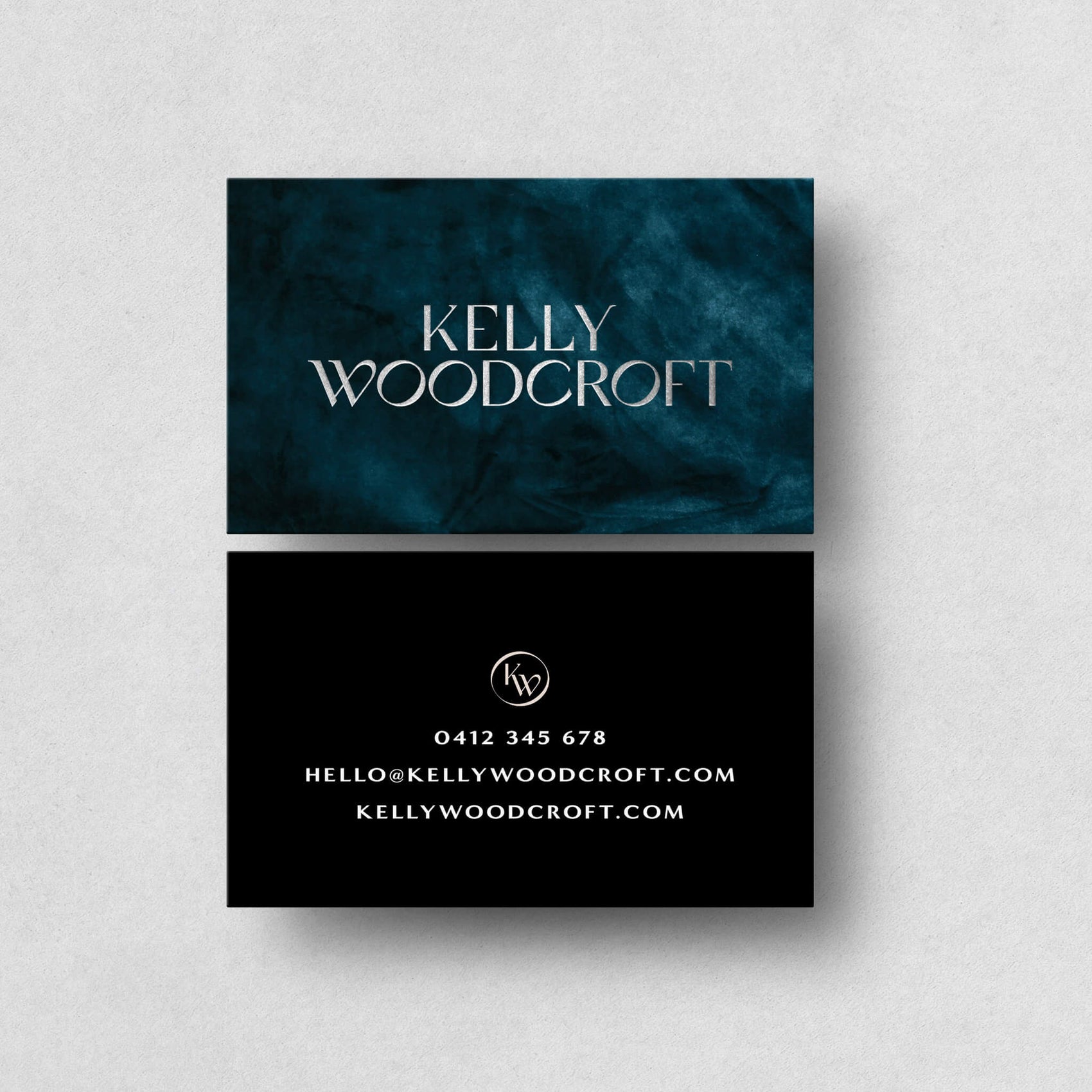 Brand design portfolio image of the Kelly Woodcroft fashion label business cards. The front shows a blue texture with the logotype in a raised silver foil while the reverse is black with white text details.