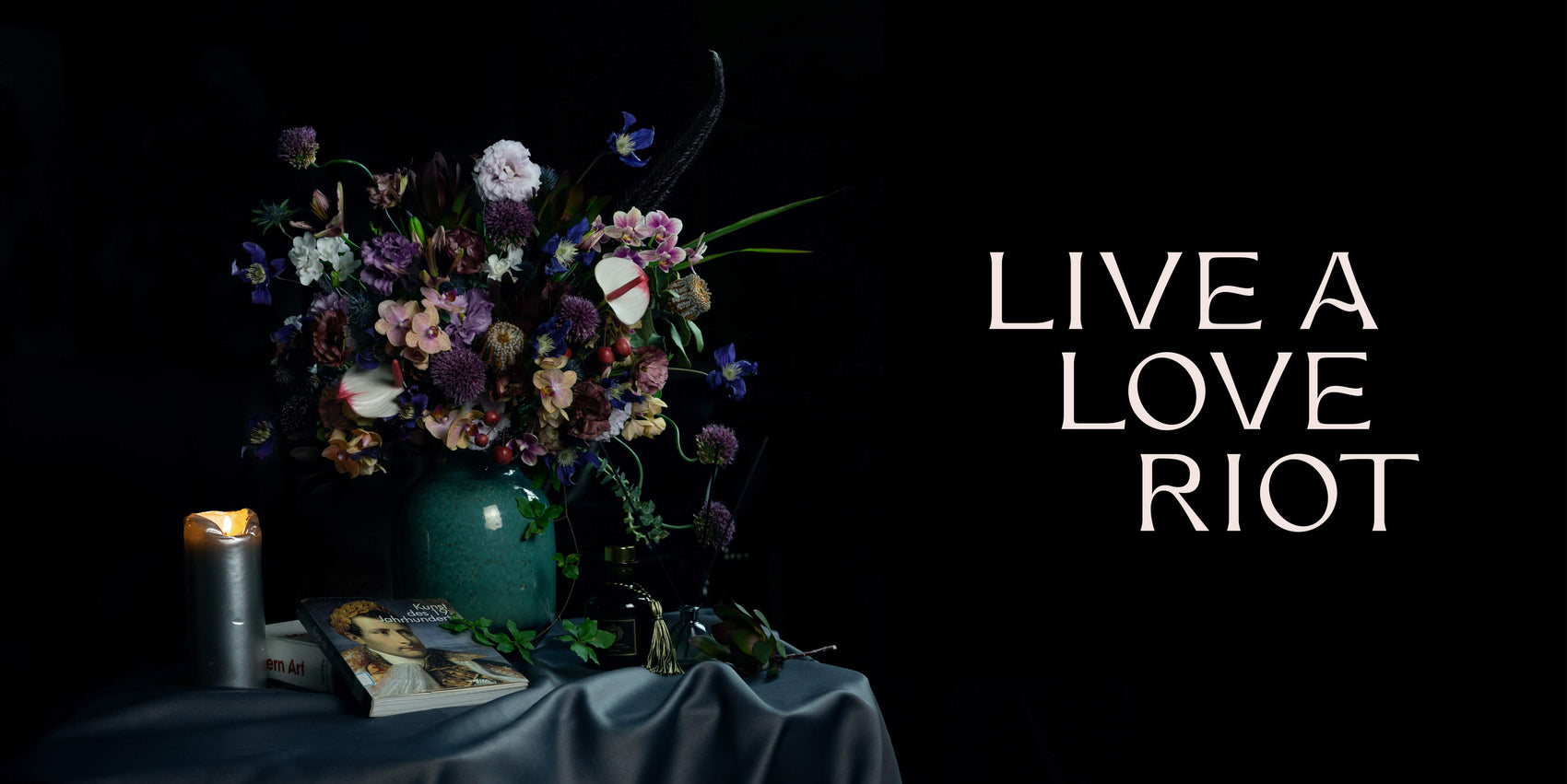 Coach branding case study image showing the Live a Love Riot brand logo. Over a dark image of an elegant bouquet, the cream logo features a mix of sharp and curved typography.