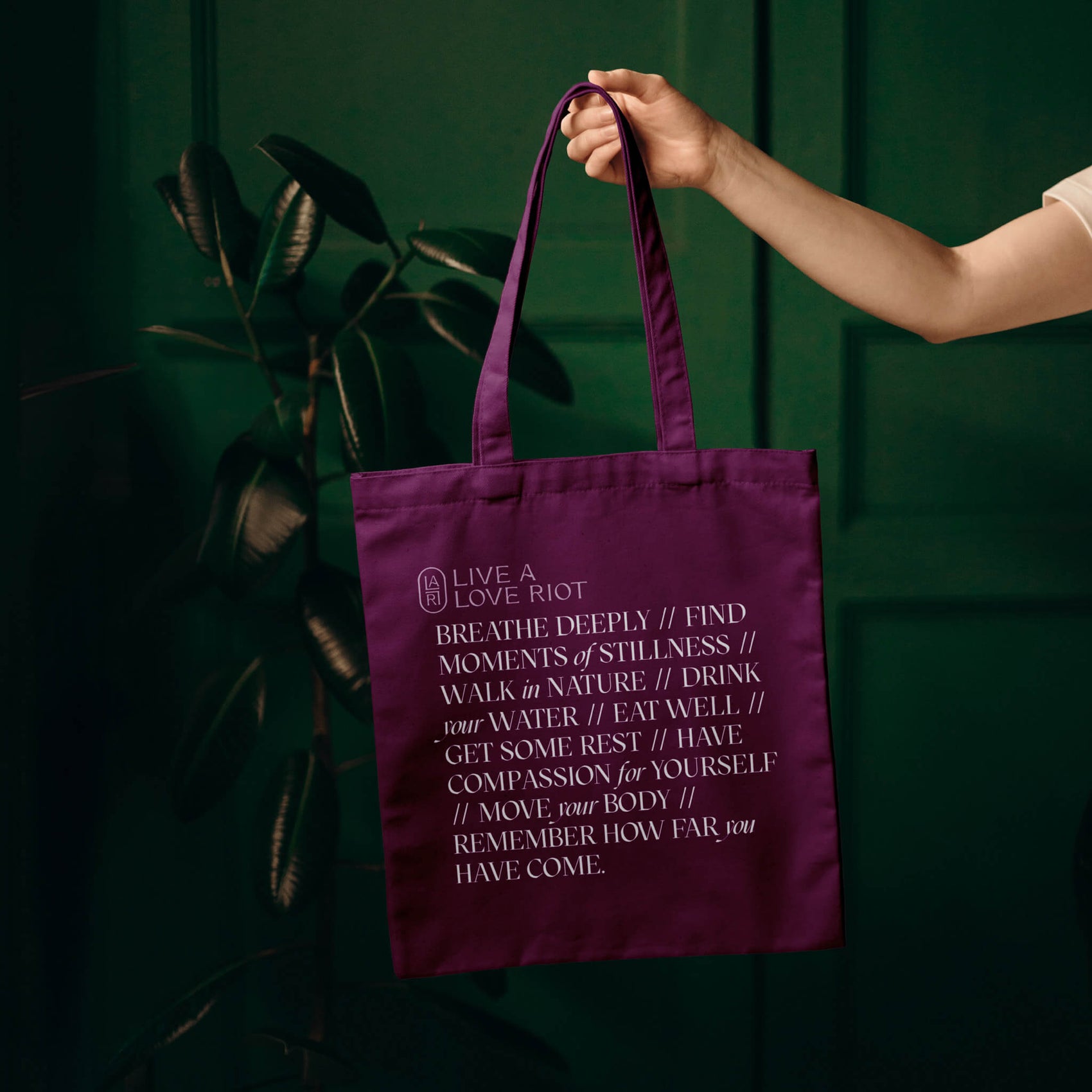 Coach branding case studies image of the Live a Love Riot tote bag. The rich purple bag features a long elegantly set quote and pink brand elements and is held in a dark green room.
