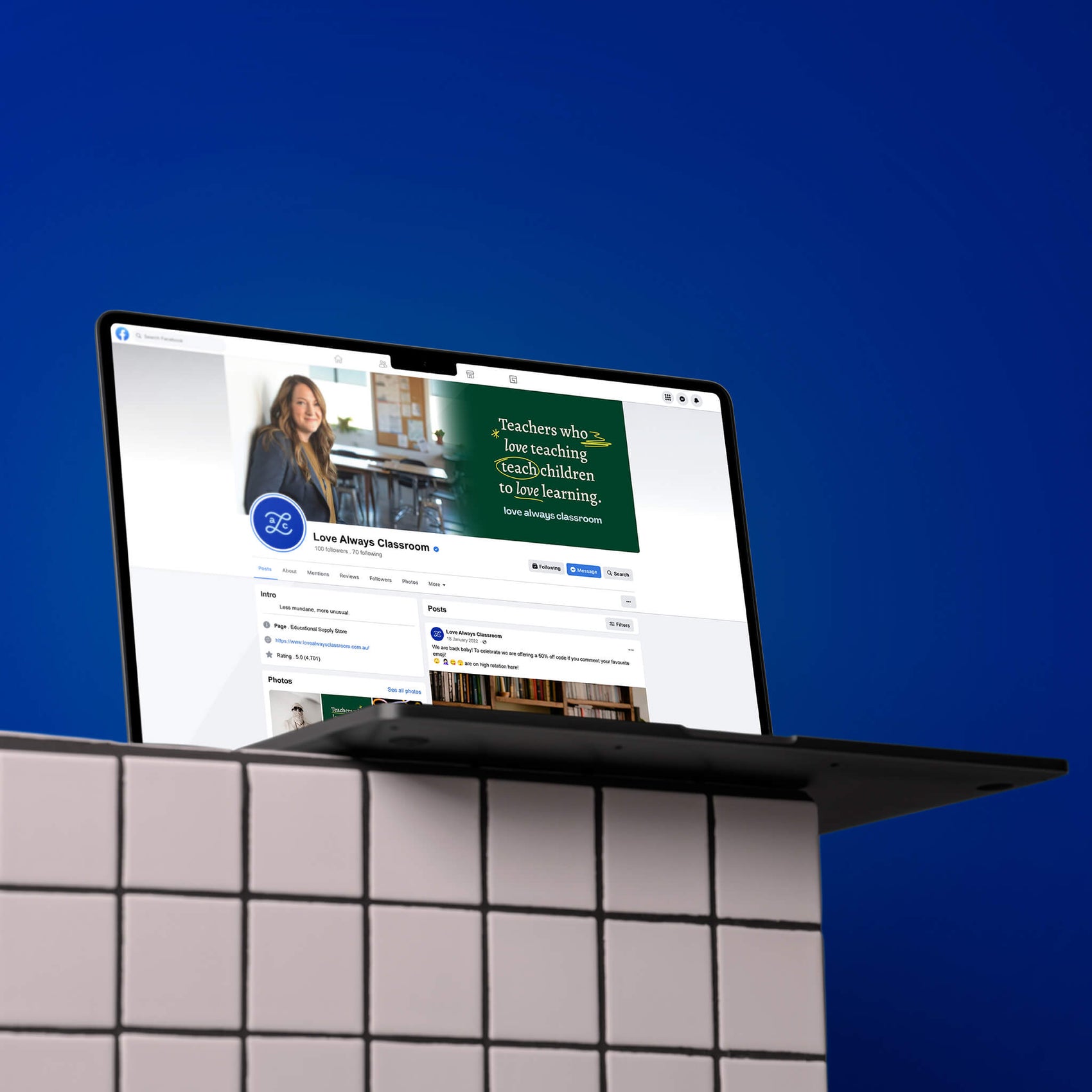 Rebranding case study image showing the Love Always Classroom retro brand identity mapped out onto a Facebook page branding. In front of a blue background, a laptop sits on a white tiled wall and shows simple brand typesetting in the custom facebook image. 