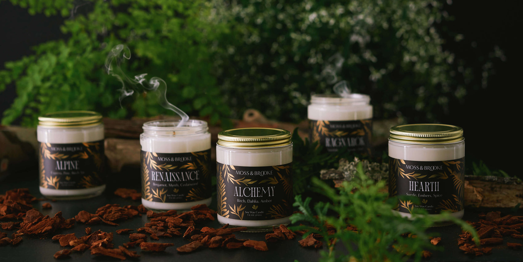 Rebranding soap case study image of Moss & Brooke range of candles in a dark moody background. The glass jars feature black labels with gold botanical detailing and ornate typography.