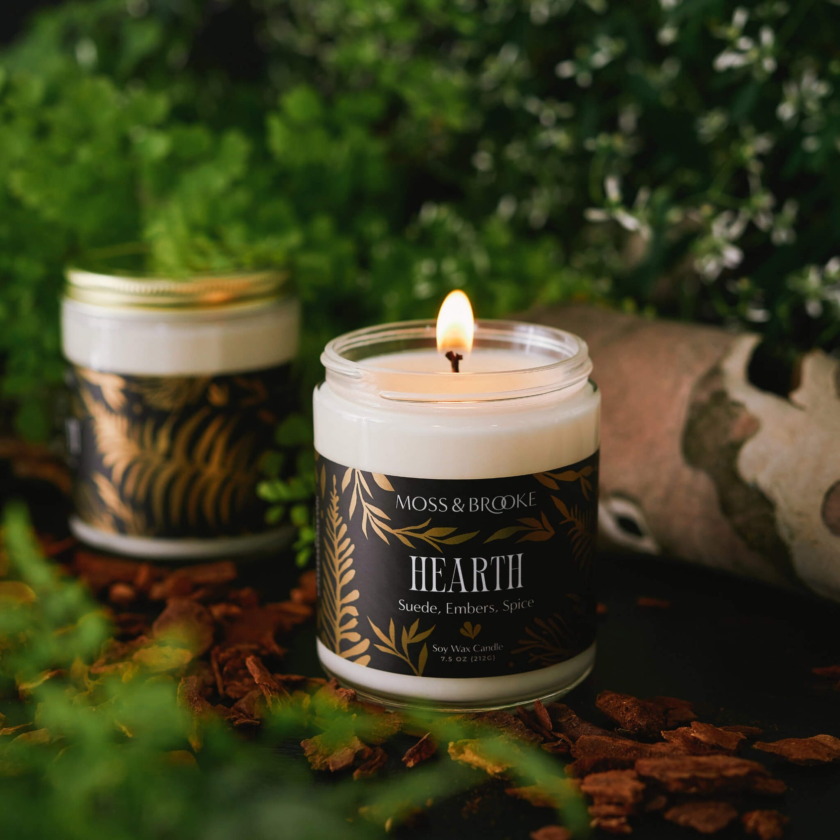 Soap rebranding case study image of Moss & Brooke range of candles in a dark moody background. The glass jars feature black labels with gold botanical detailing and ornate typography.