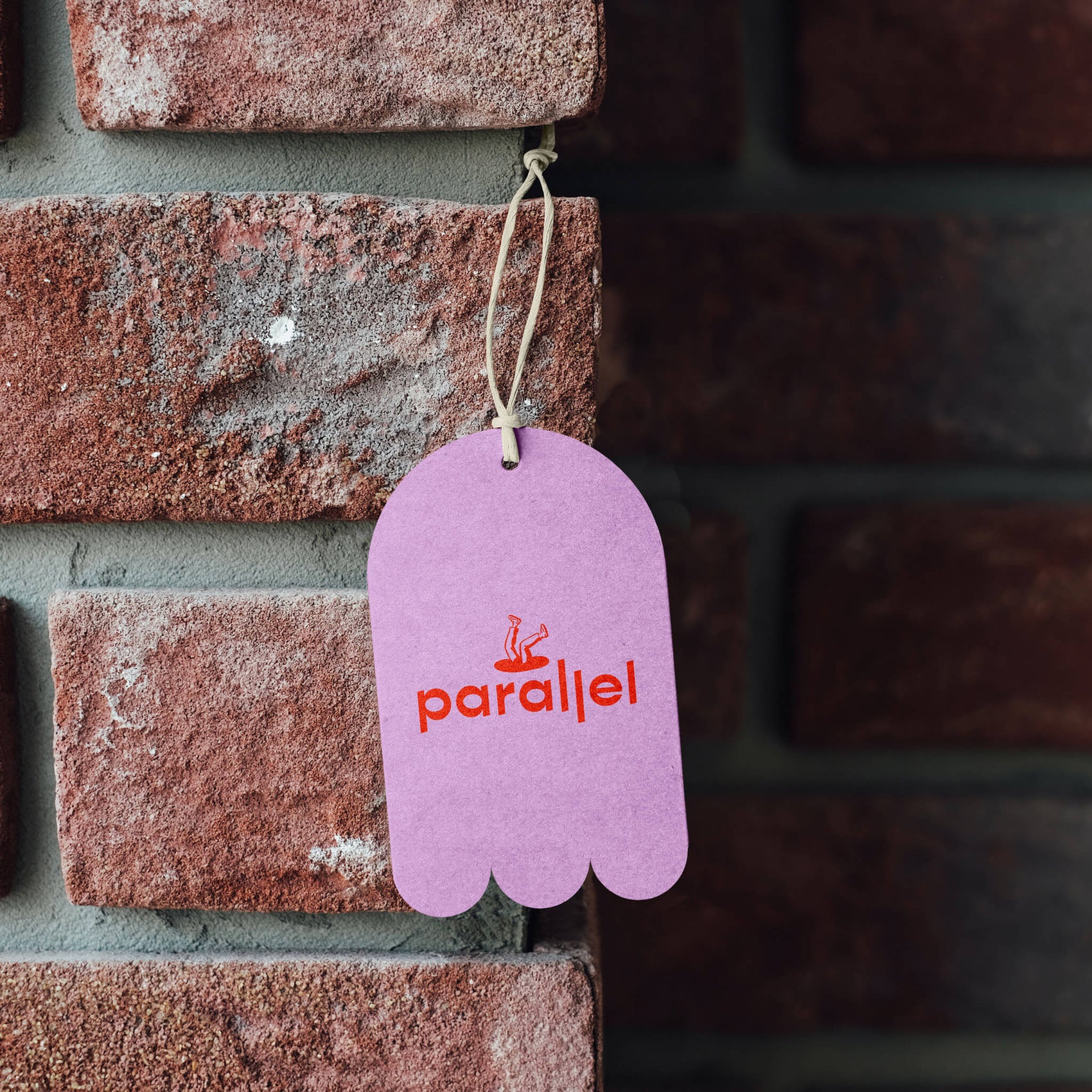Coffee House rebranding case study image of Parallel swing tag on a brick wall. The tag is bright pink with a red logo as well as a custom-dieline in a blobby shape.
