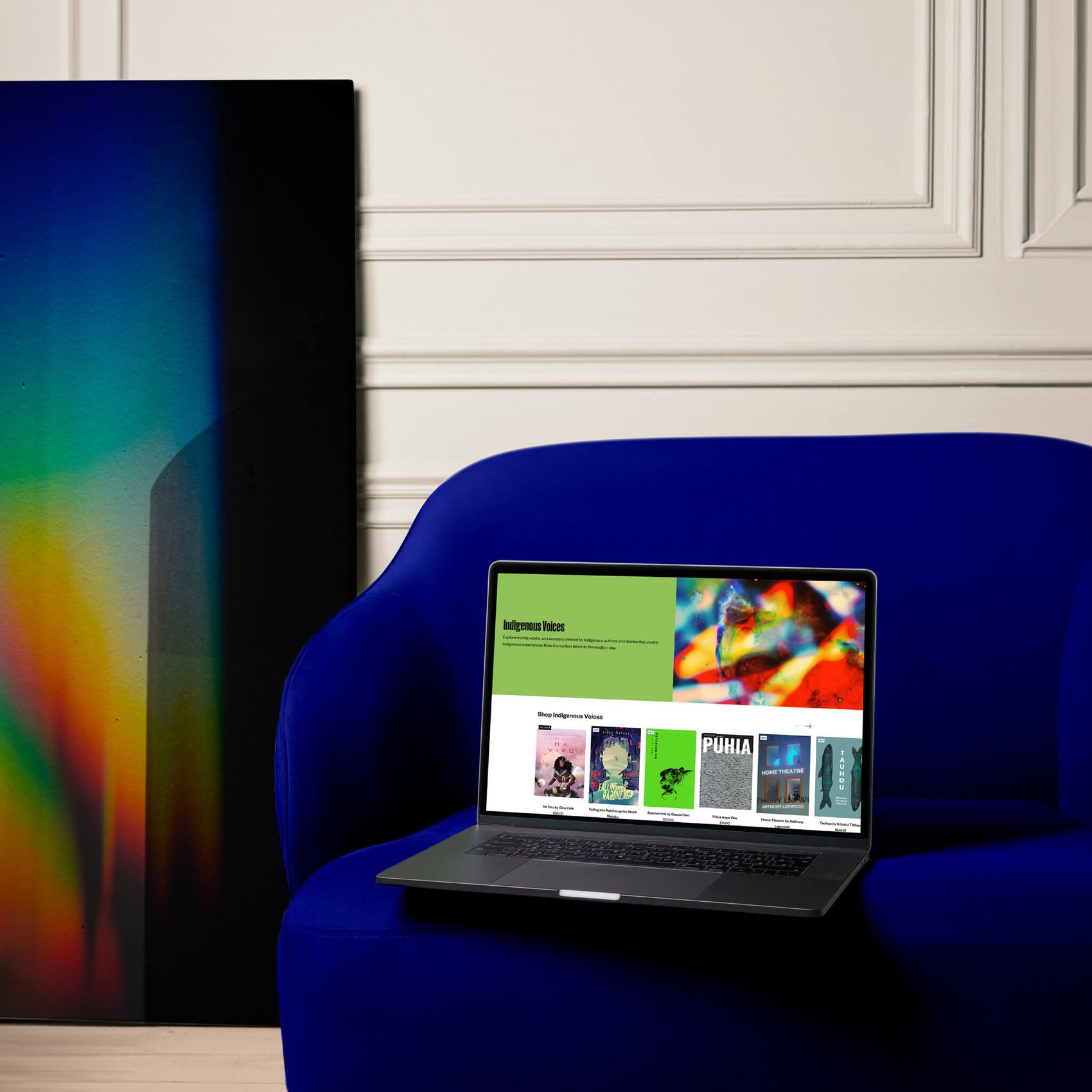 Bookstore brand identity case study image of the Parallel Shopify website design shown on a laptop. The laptop sits in a white room on a deep blue chair next to a dark artwork featuring a rainbow light flair. 