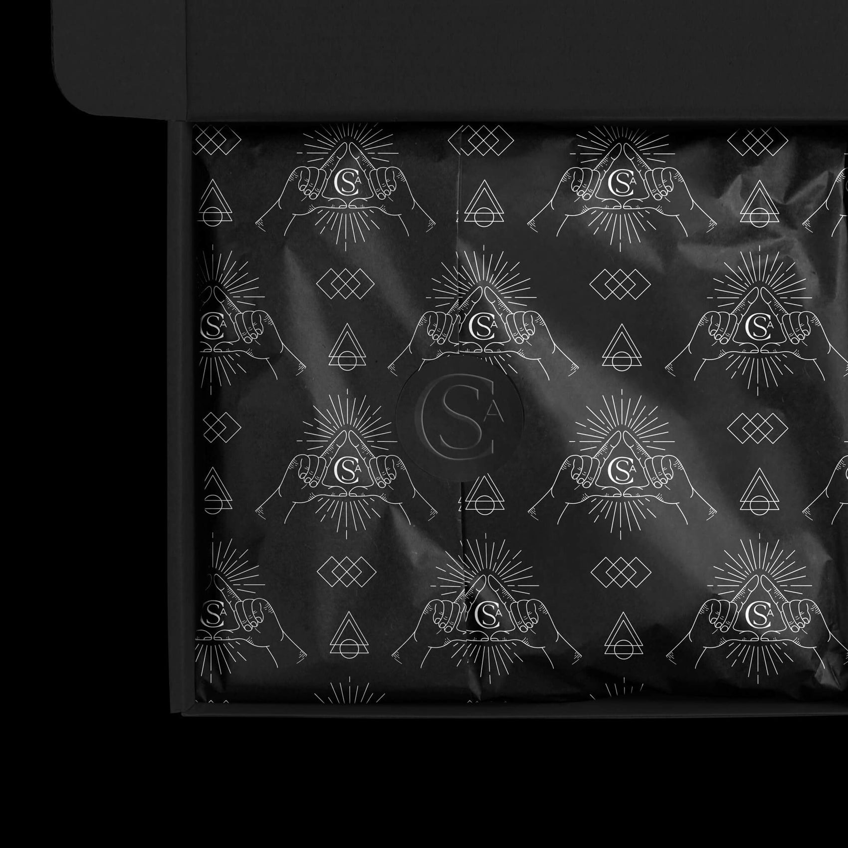 Skincare brand identity case study image of the Soap Cult Australia custom tissue paper design. The black paper features white imager of geometric shapes as well as the brand seal. An embossed sticker in all black seals the package. 