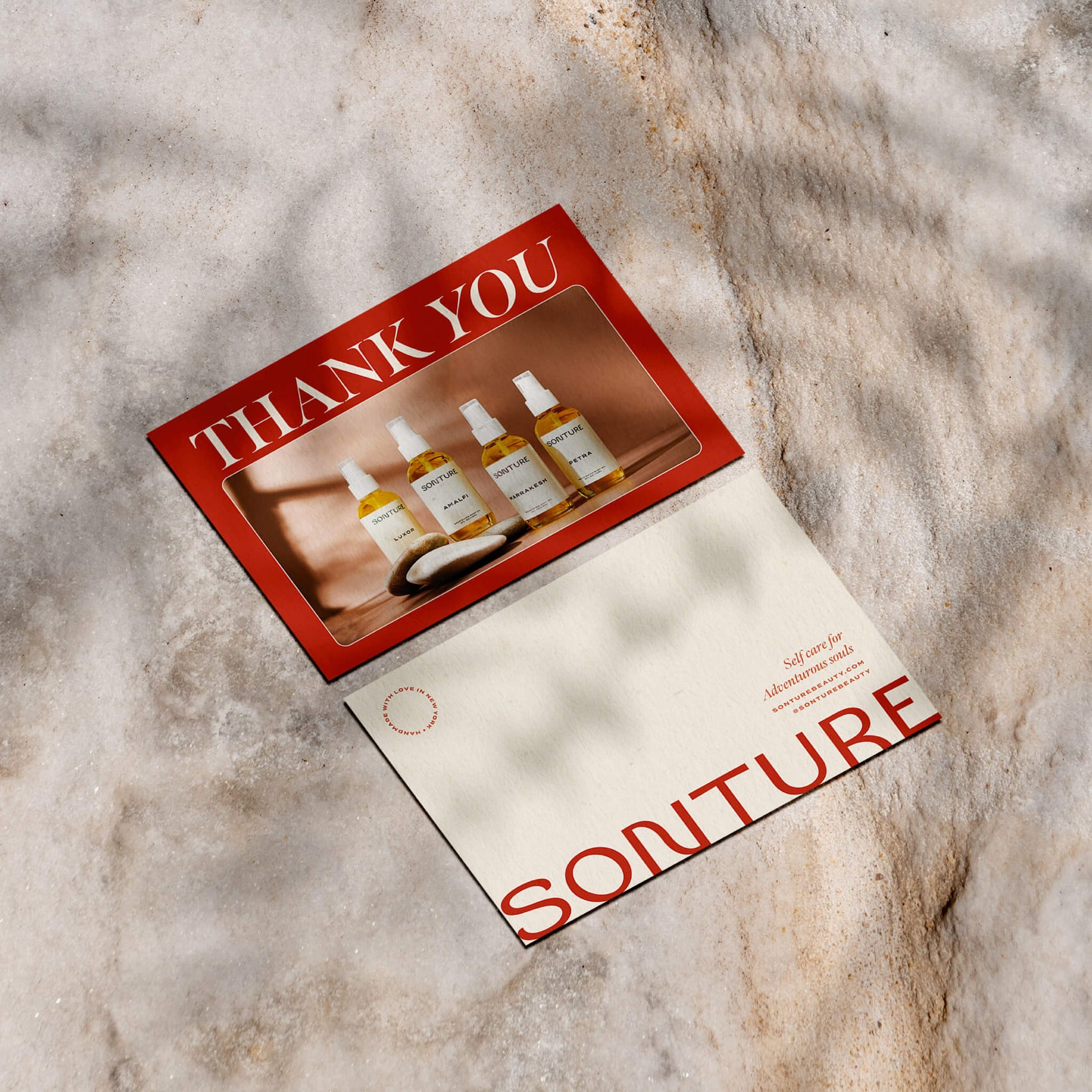 Soap brand designer portfolio image of the Sonture custom thank you cards sitting on a stone. Bold red, the brand photography and sharp typography feels elegant with the back styled to look like a postcard. 