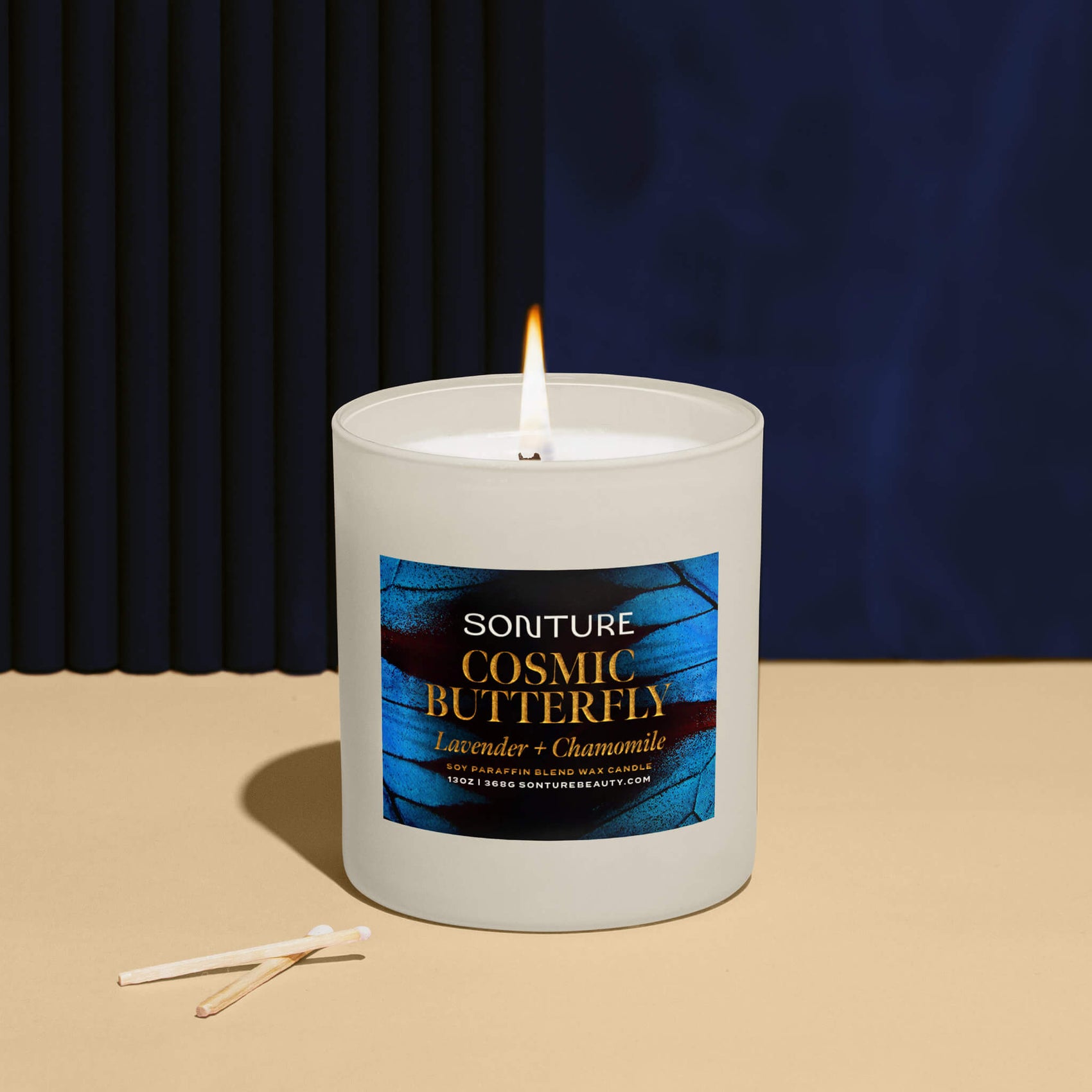 Brand design portfolio image of the Sonture candle packaging sitting in a deep blue room. The white glass candle features a colourful label with a macro image of a butterfly and sophisticated gold foil packaging detailing. 