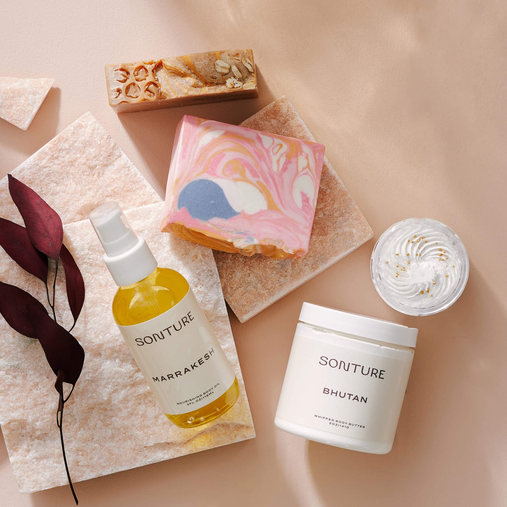 Soap branding case study image of the Sonture product range. On a pink background sits a body oil, soaps, body scrub and body butter alongside a quartz stone. 