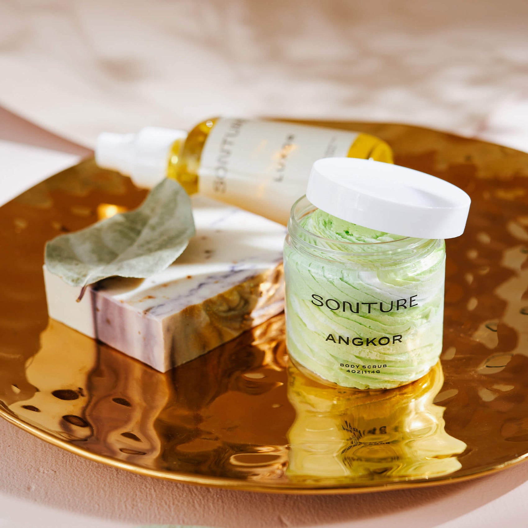 Skincare brand design portfolio image of the Sonture body butter, soap and oil on a gold tray in an elegant setting. The very minimal label creates a minimal, high end feel. 