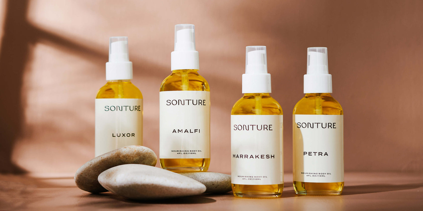 Candle branding case study image of the Sonture range of body oil. The minimally labelled glass bottles sit in a neutral room with shadows and river pebbles for styling. 