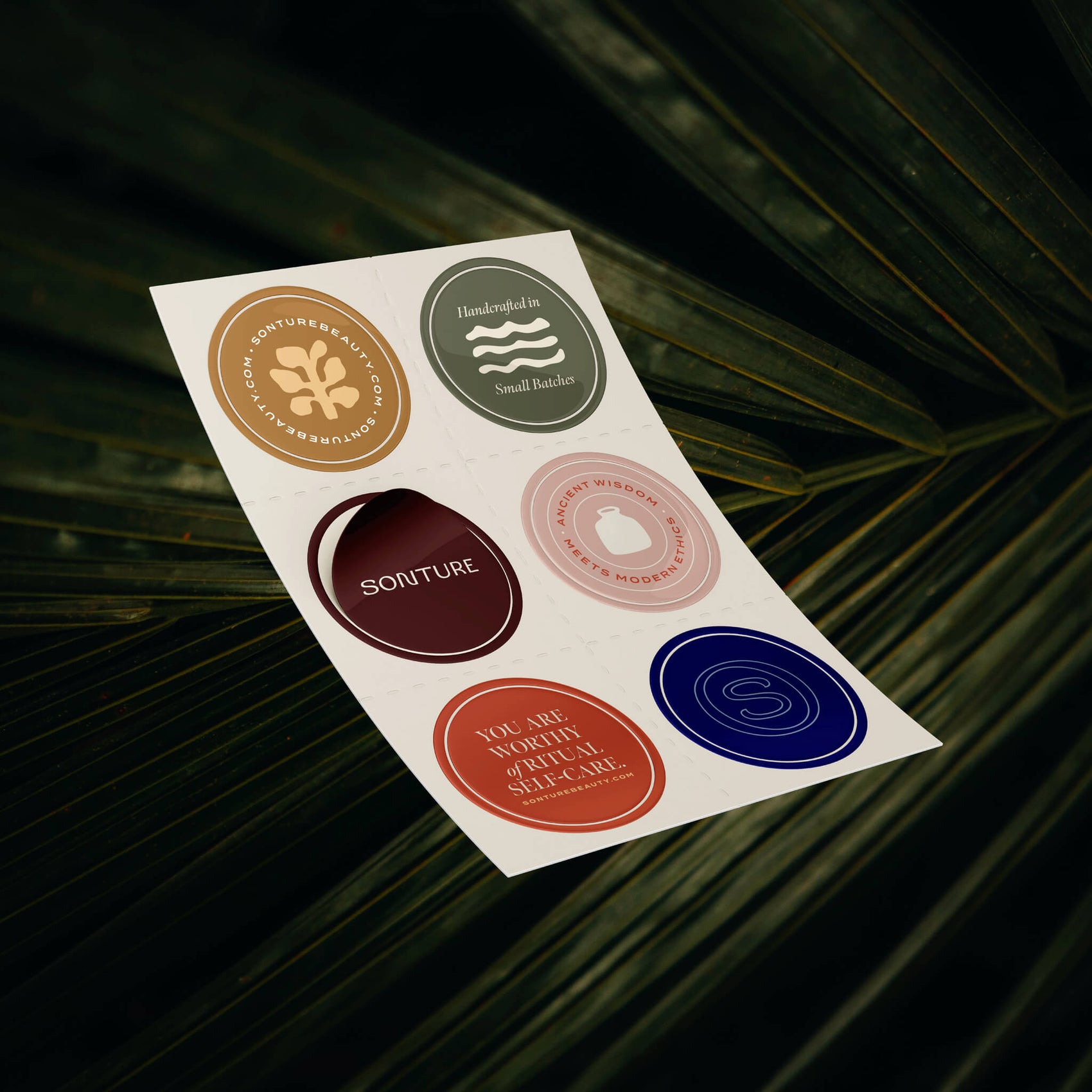 Soap branding case study image of the Sonture branded sticker sheet in a lush green background. The stickers feature the various brand logos and taglines as well as the high end colour palette.