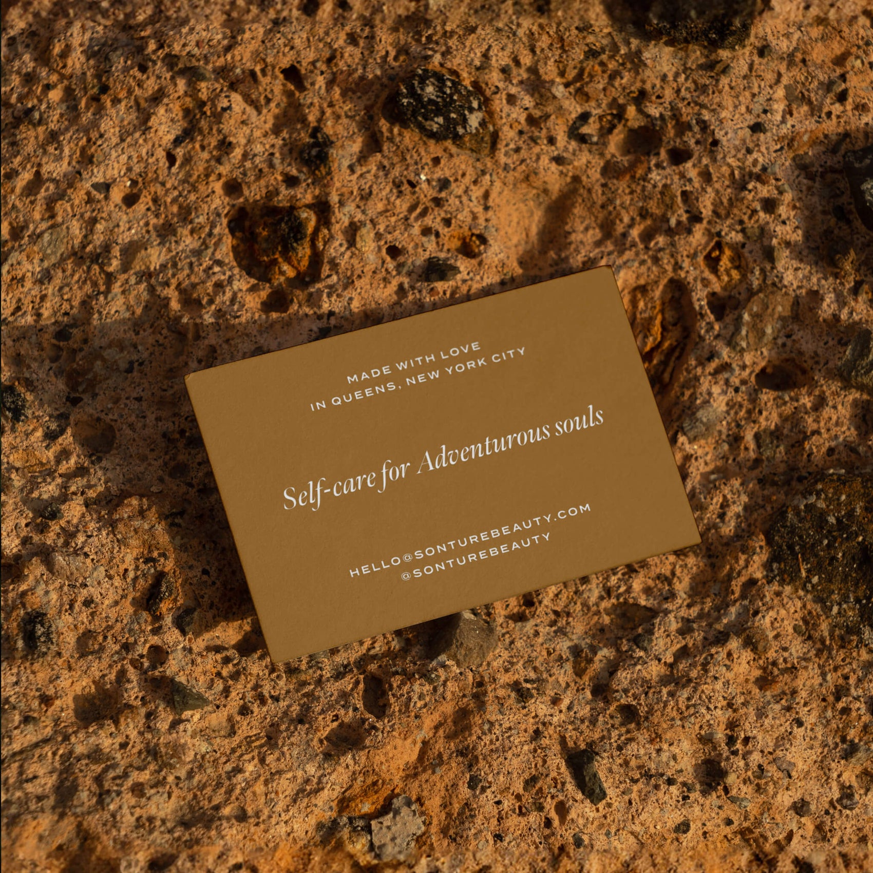 Brand designer portfolio image of the Sonture business card sitting on a rocky surface. The brown coloured card features white matte foil detailing and elegant typography. 