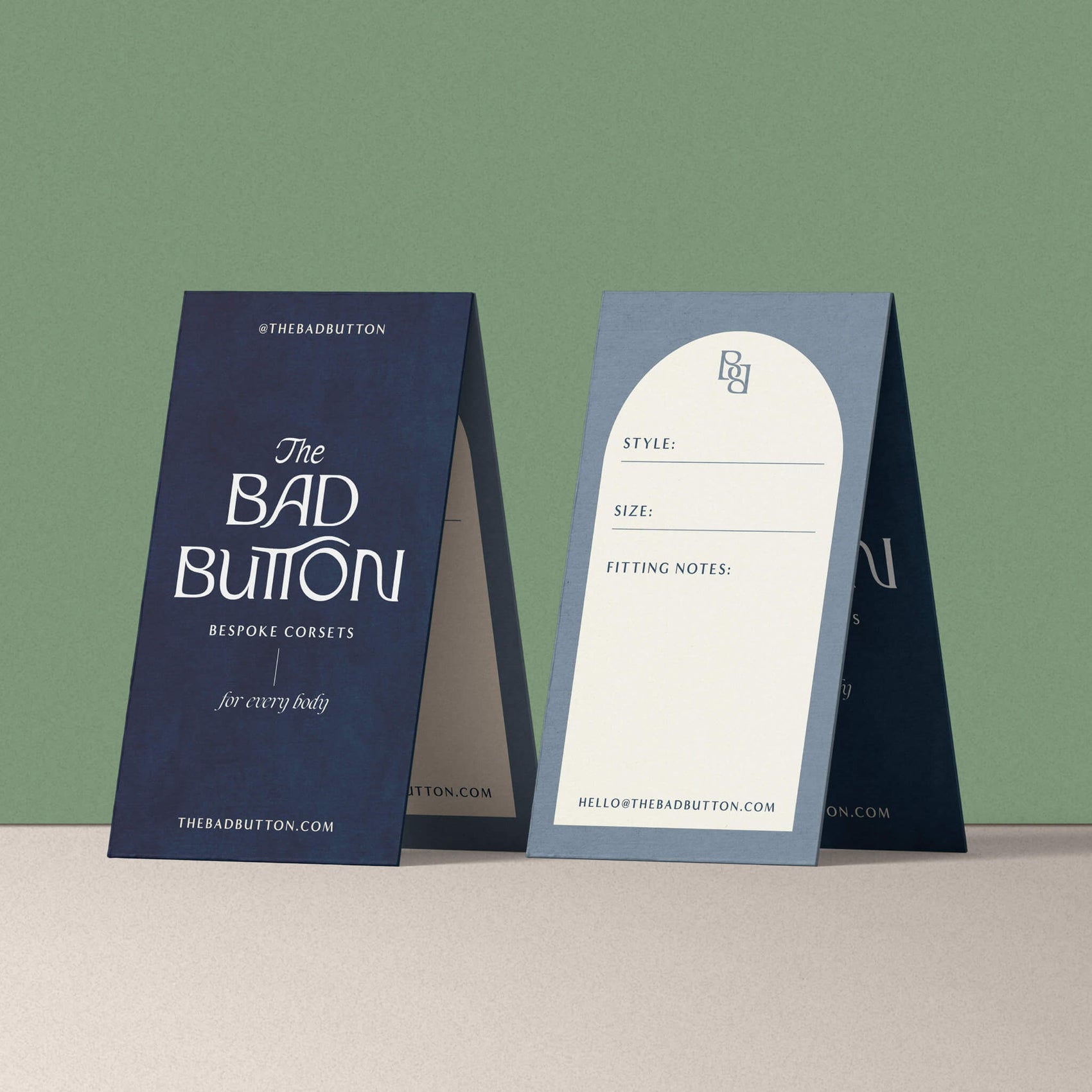 Brand identity case study image of The Bad Button fitting cards sit in a mint green setting. The dusty blue cards feature the full brand logo on the front with the back having a cream coloured arch and space for details to be filled out.