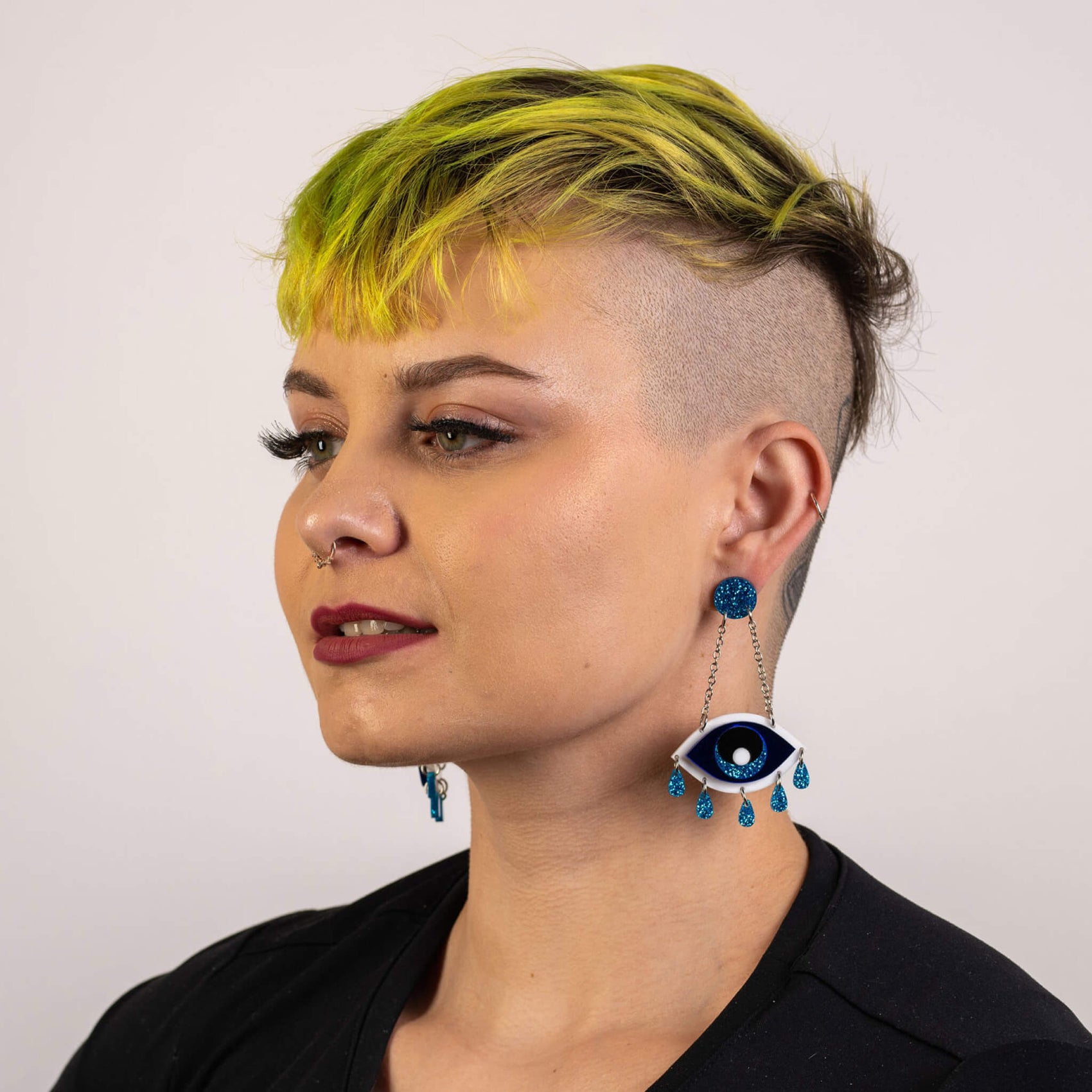 Rebranding case study image of one of The Bad Button product images. A woman with yellow hair with shaved sides wears acrylic eye shaped earrings. 