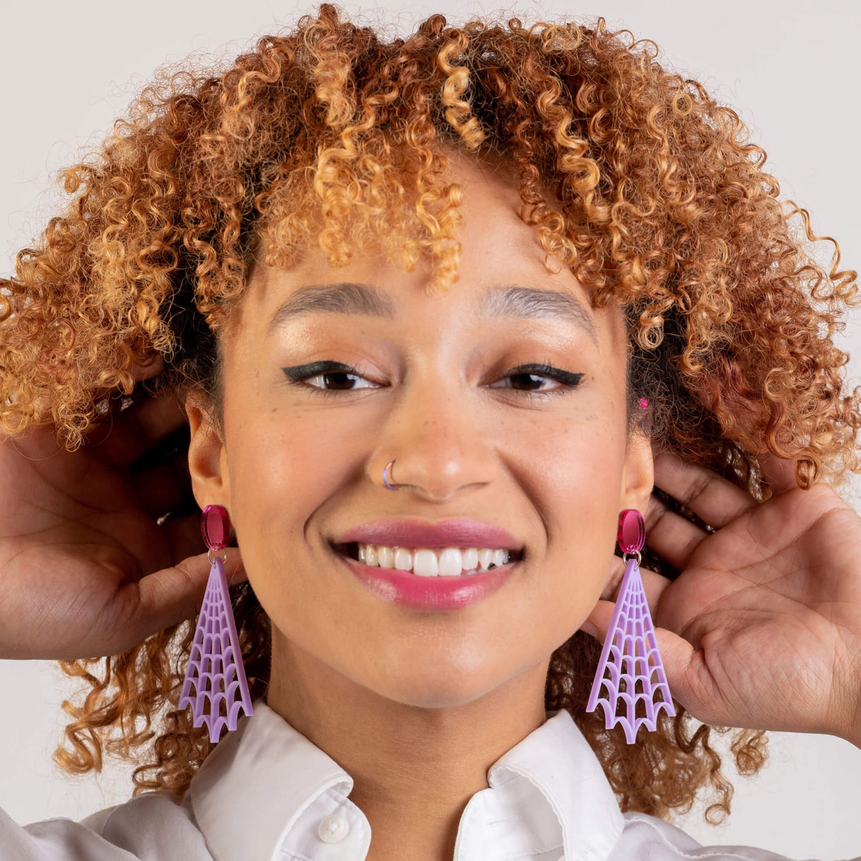 Rebranding case study image of one of The Bad Button product images. A woman with curly hair wears acrylic purple and pink spider web shaped earrings. 