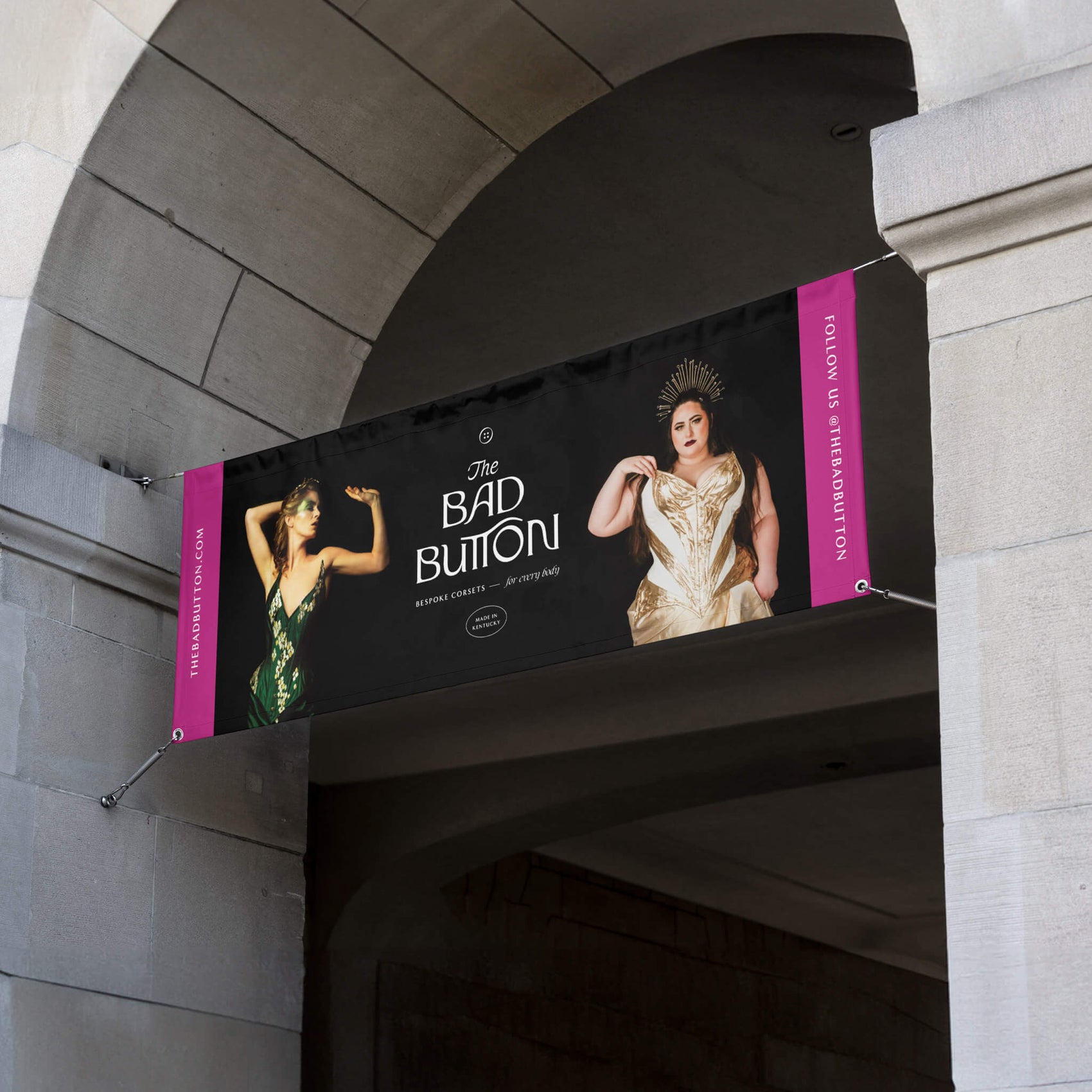 Fashion label brand Designer Portfolio image of The Bad Button banner on a brick building. The artwork shows two images of women in corsets and the brand logo on a black background with the URL and social details in bright pink sections on either side. 