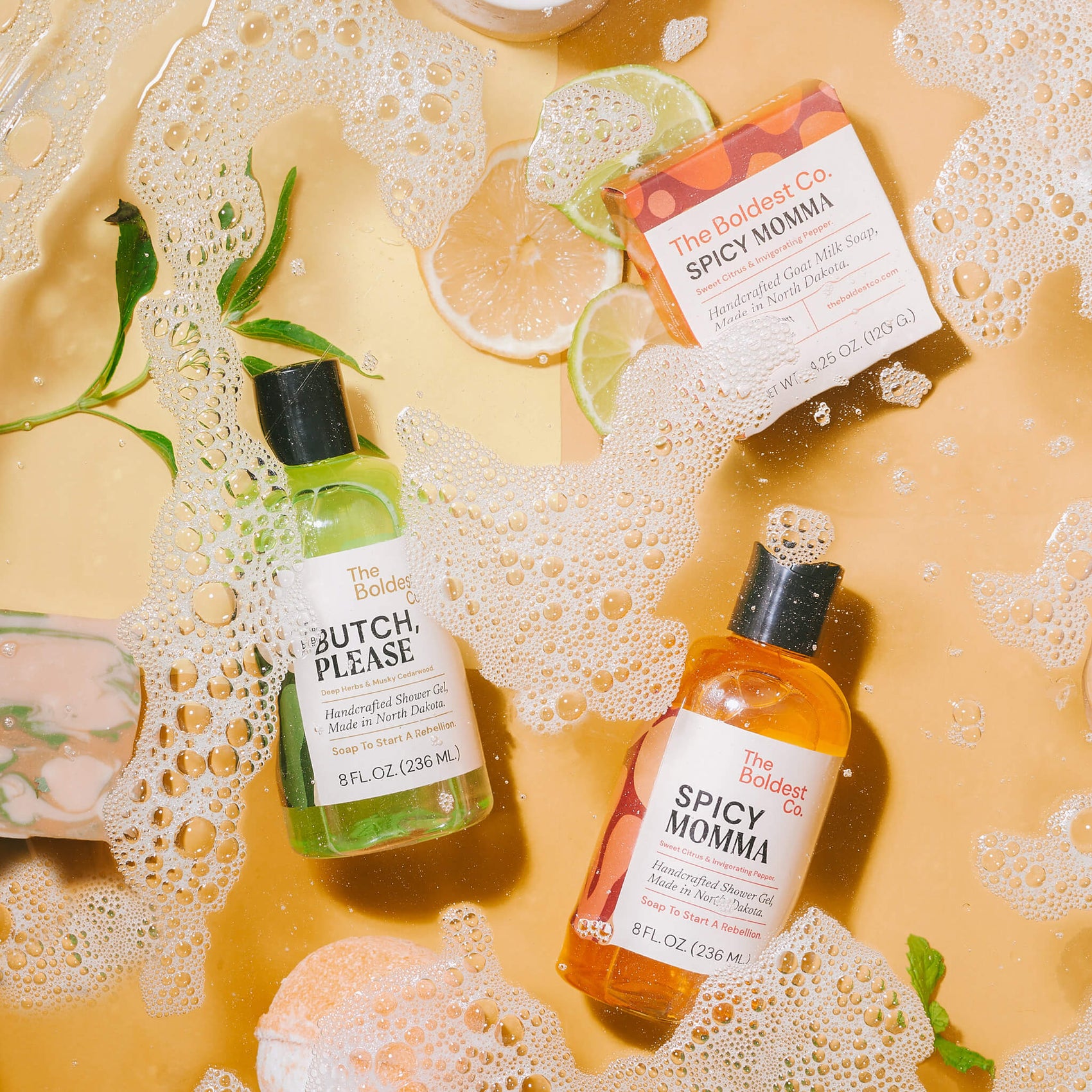 Soap brand design portfolio styled image of The Boldest Co’s full range of products. A soap box, shower gel, hand wash and bath bomb are submerged under slightly soapy water. 