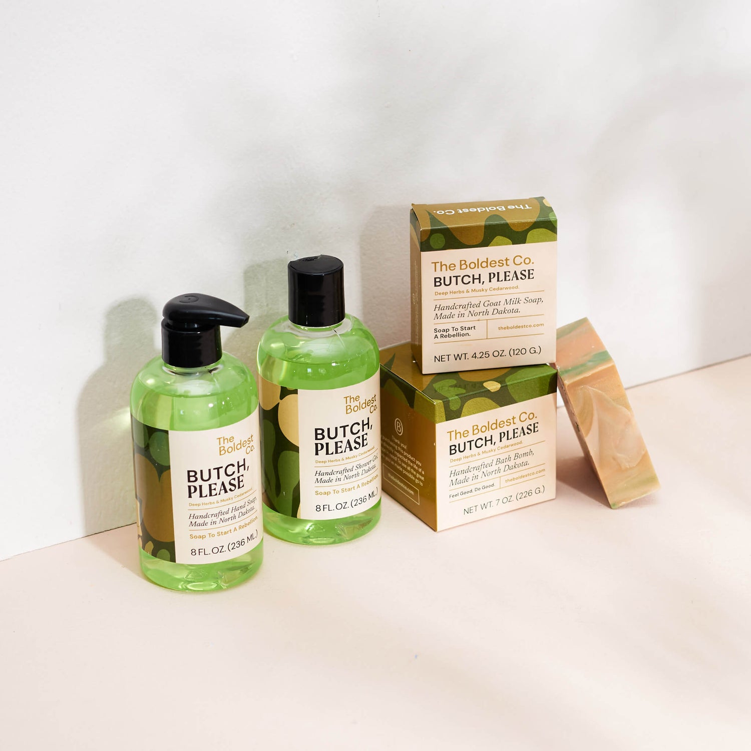 Brand identity case study image of The Boldest Co’s ‘Butch, Please’ scent range. A hand wash, shower gel, soap box and bath bomb box feature green detailing and sit in a cream coloured background.