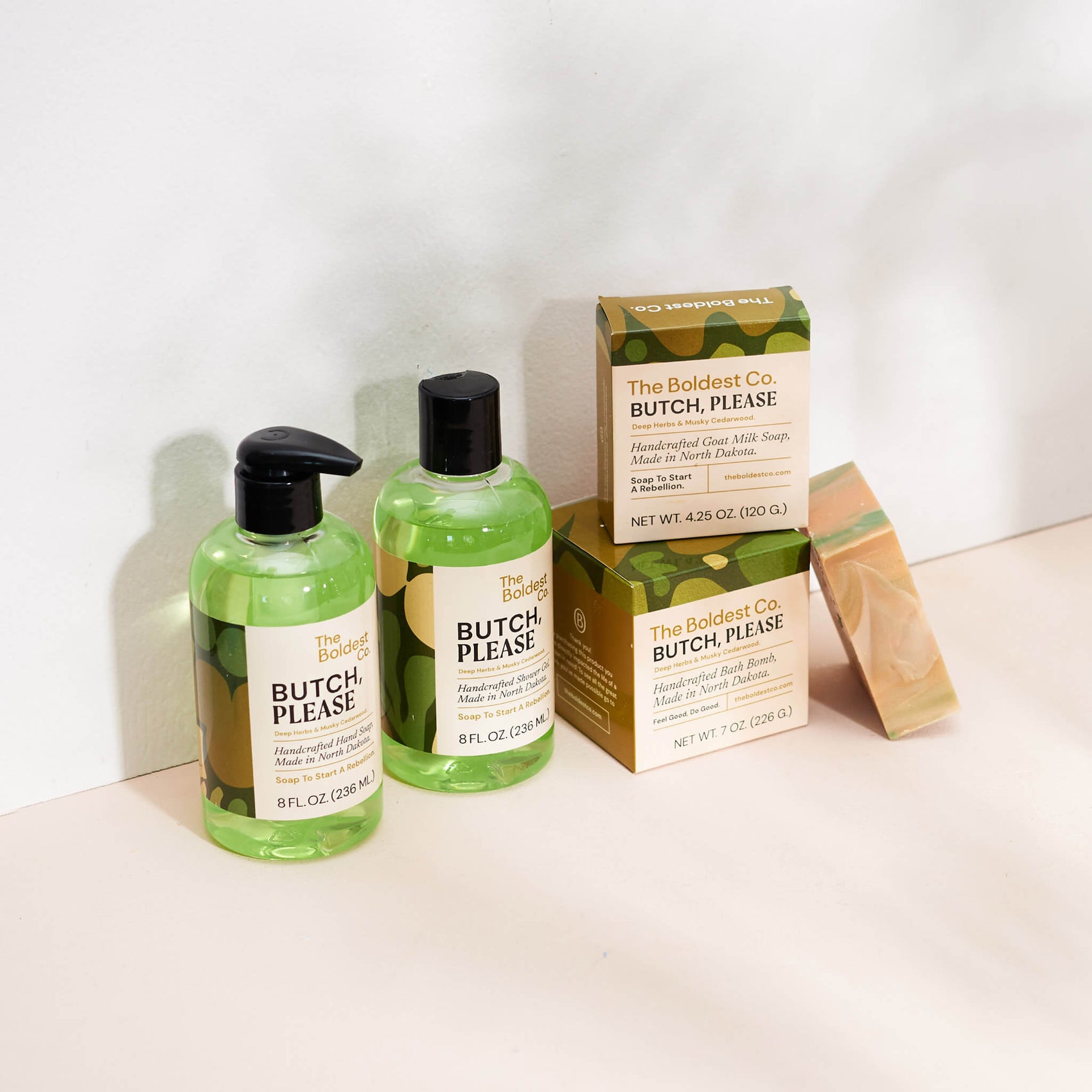 Brand identity case study image of The Boldest Co’s ‘Butch, Please’ scent range. A hand wash, shower gel, soap box and bath bomb box feature green detailing and sit in a cream coloured background.