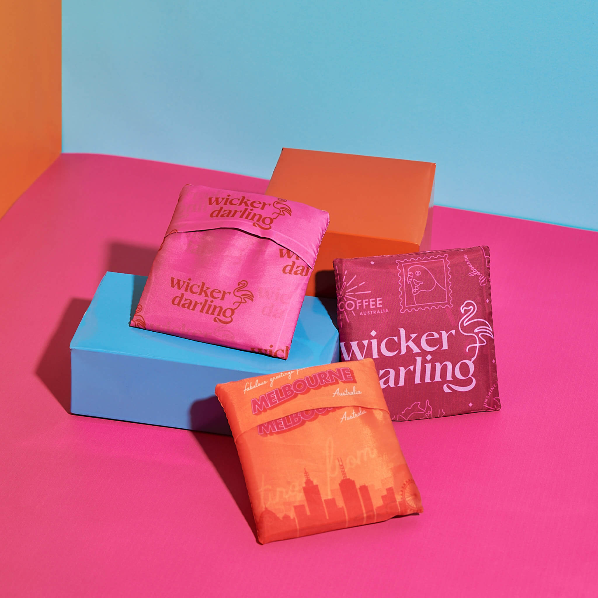Handbag brand design portfolio image of custom designed tote bags for Wicker darling. In a pink and blue room the three folded bags sit. They each feature tropical colours of pink, purple and bright orange.