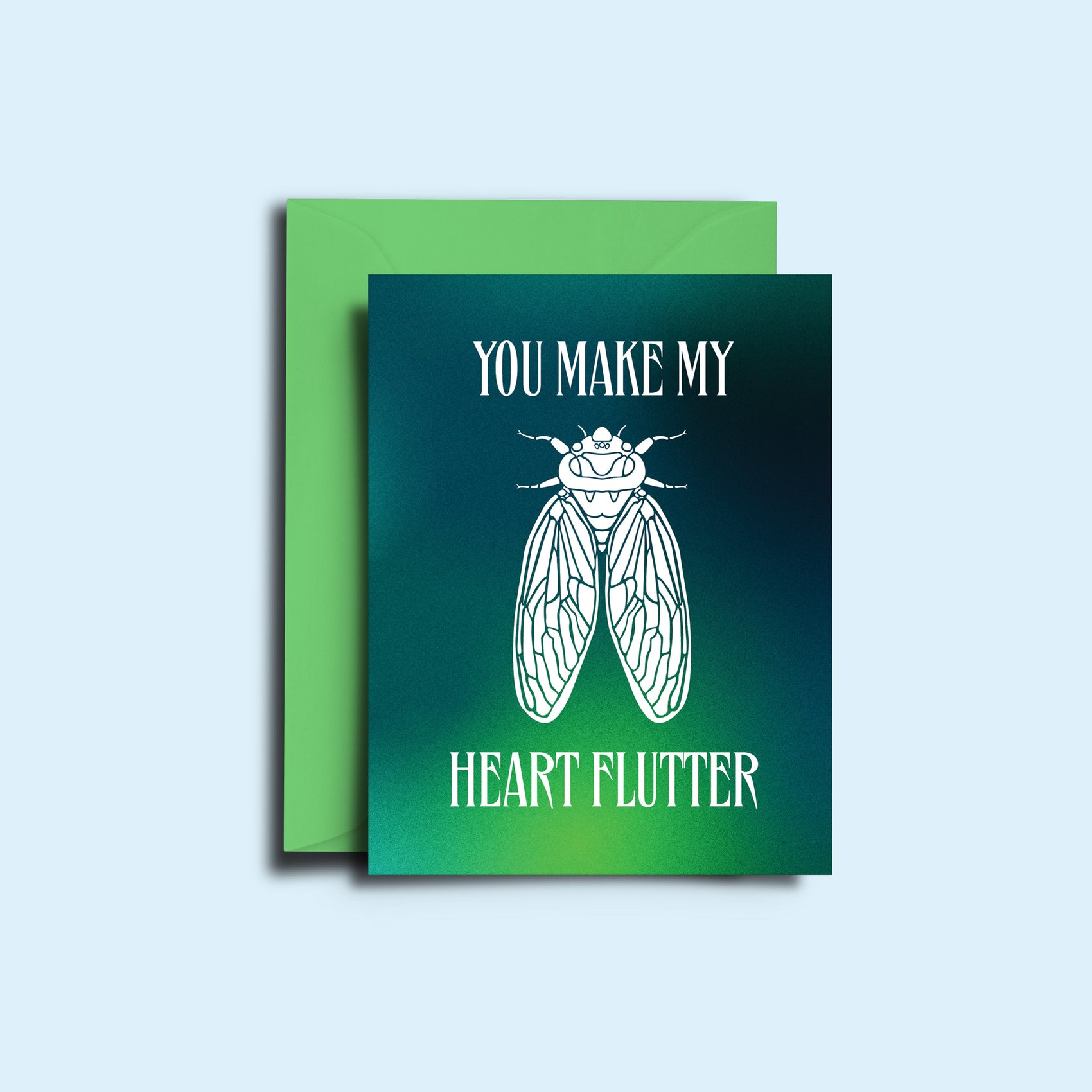 An image of the cicada 'you make my heart flutter' greeting card alongside it's green envelope. The card features a hazy green gradient with the sharp copy and illustration of a cicada in white.  