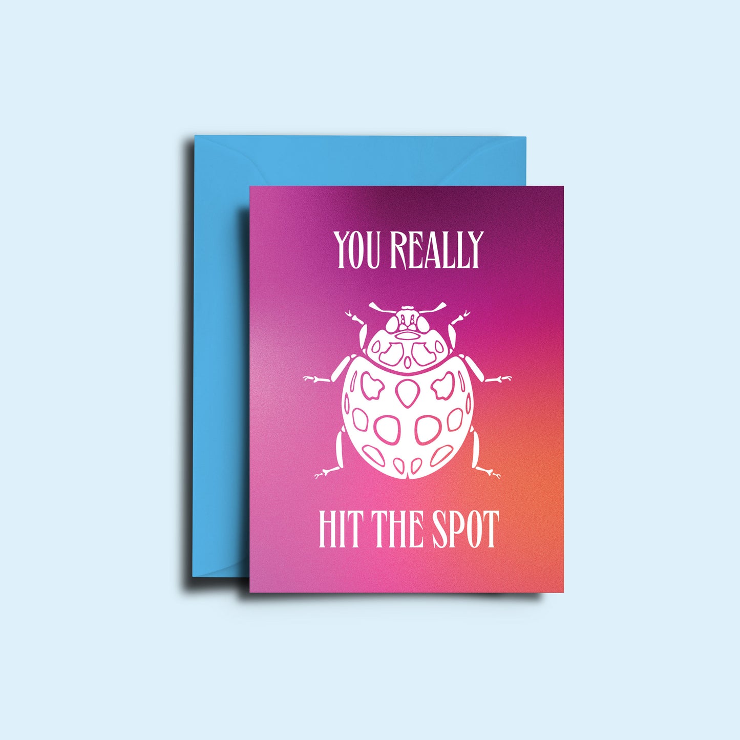 An image of the ladybird 'you really hit the spot' greeting card alongside it's bright green envelope. The card features a hazy pink gradient with the sharp copy and illustration of a ladybug in white.  