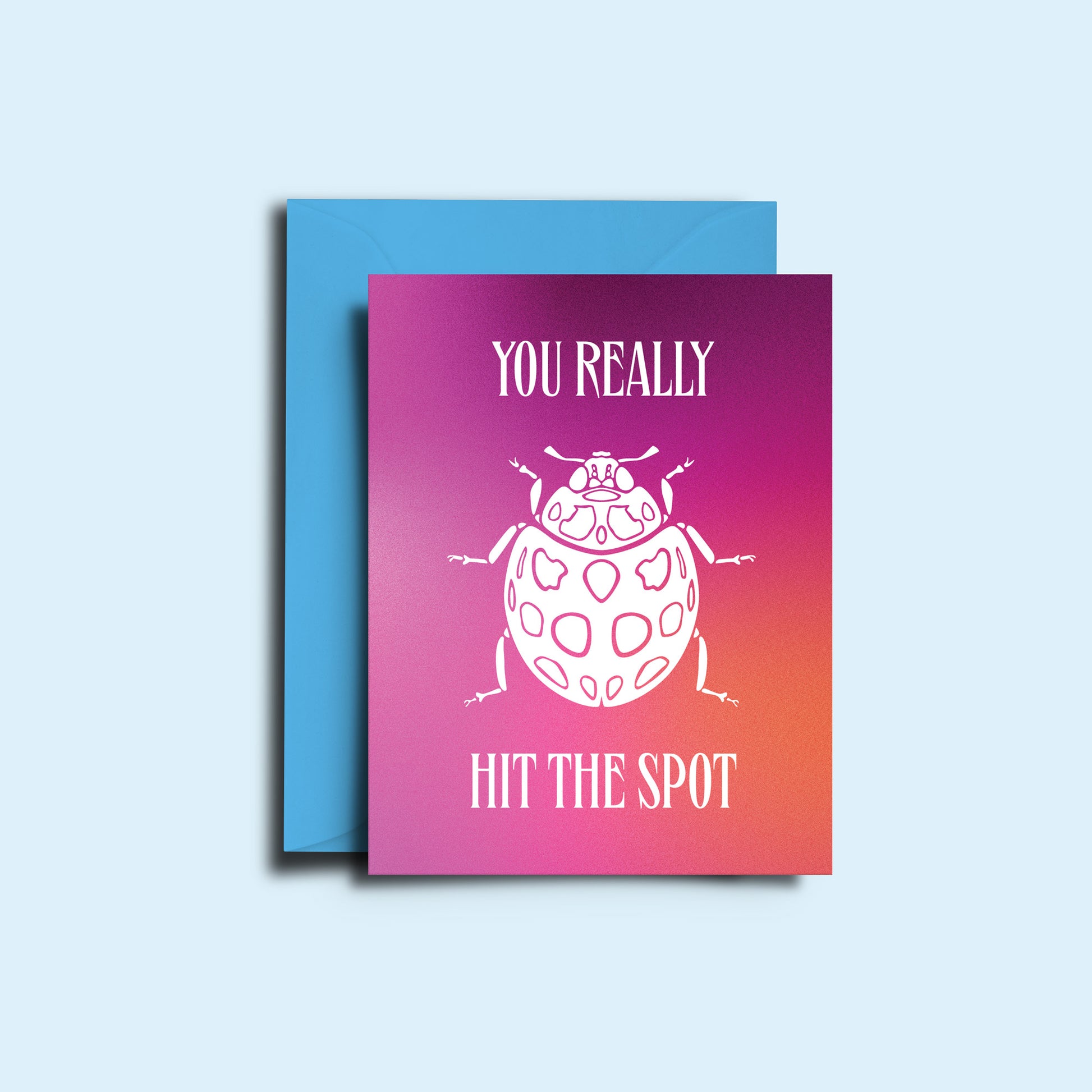 An image of the ladybird 'you really hit the spot' greeting card alongside it's bright green envelope. The card features a hazy pink gradient with the sharp copy and illustration of a ladybug in white.  
