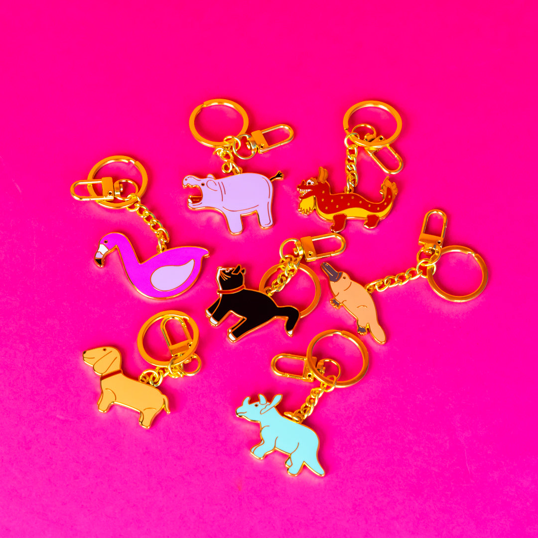 Fashion label branding design image of a Wicker Darling custom enamel keyring design. On a pink background sits the range of gold keyrings inspired by the wicker bag designs. 